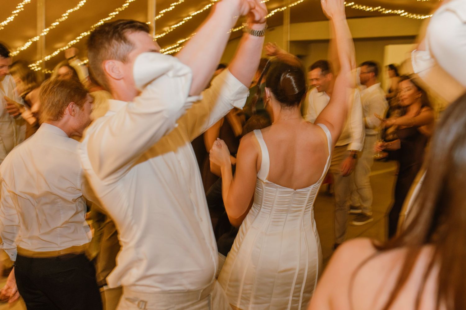 Wedding celebration with guests dancing under string lights.