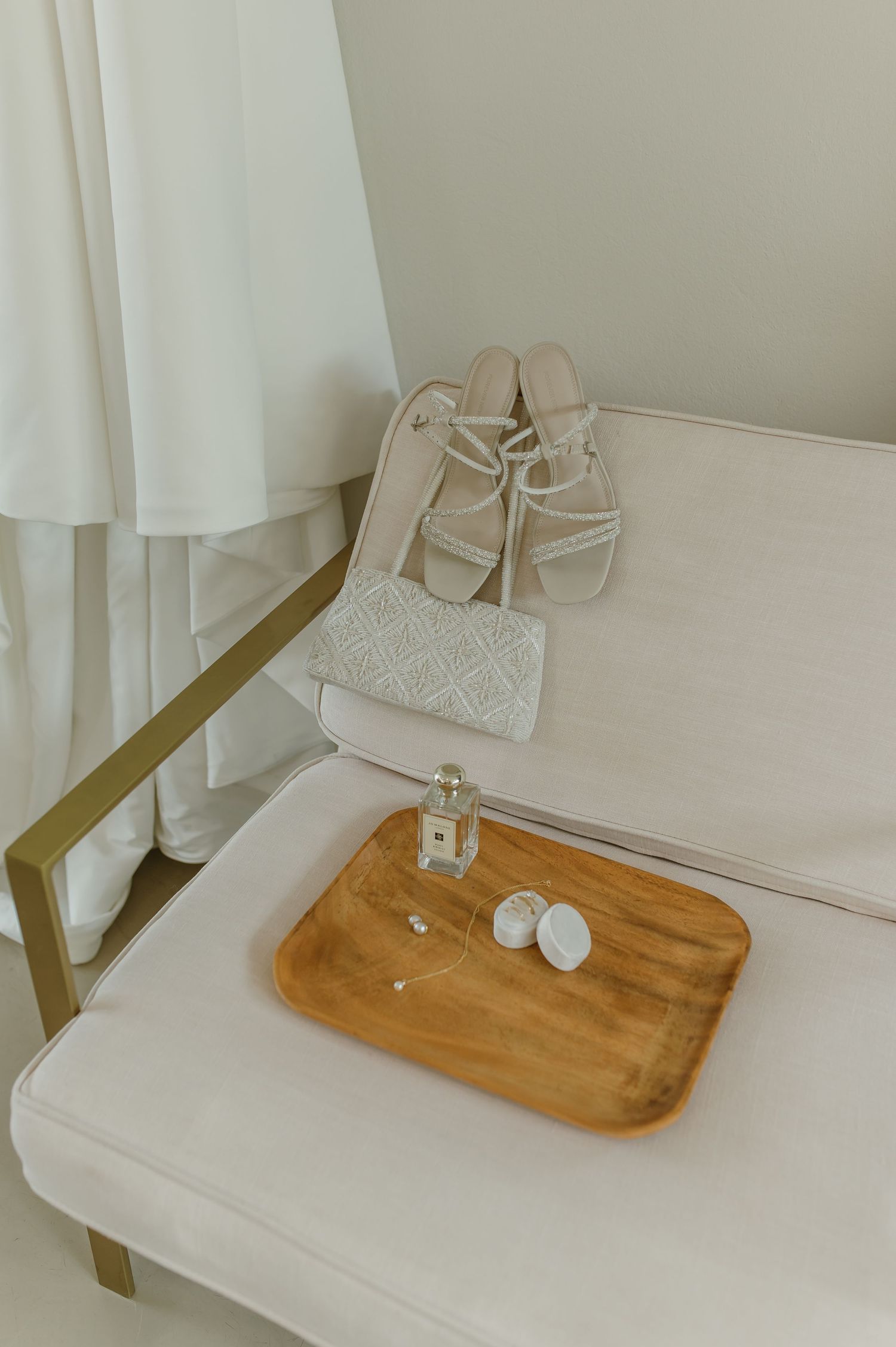Minimalist scene with sandals and wooden tray on white couch with gold accents.