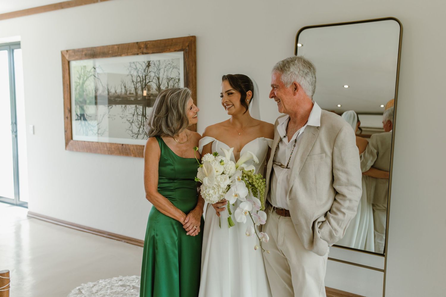 Wedding party members help with final preparations in a bright room with mirrors.