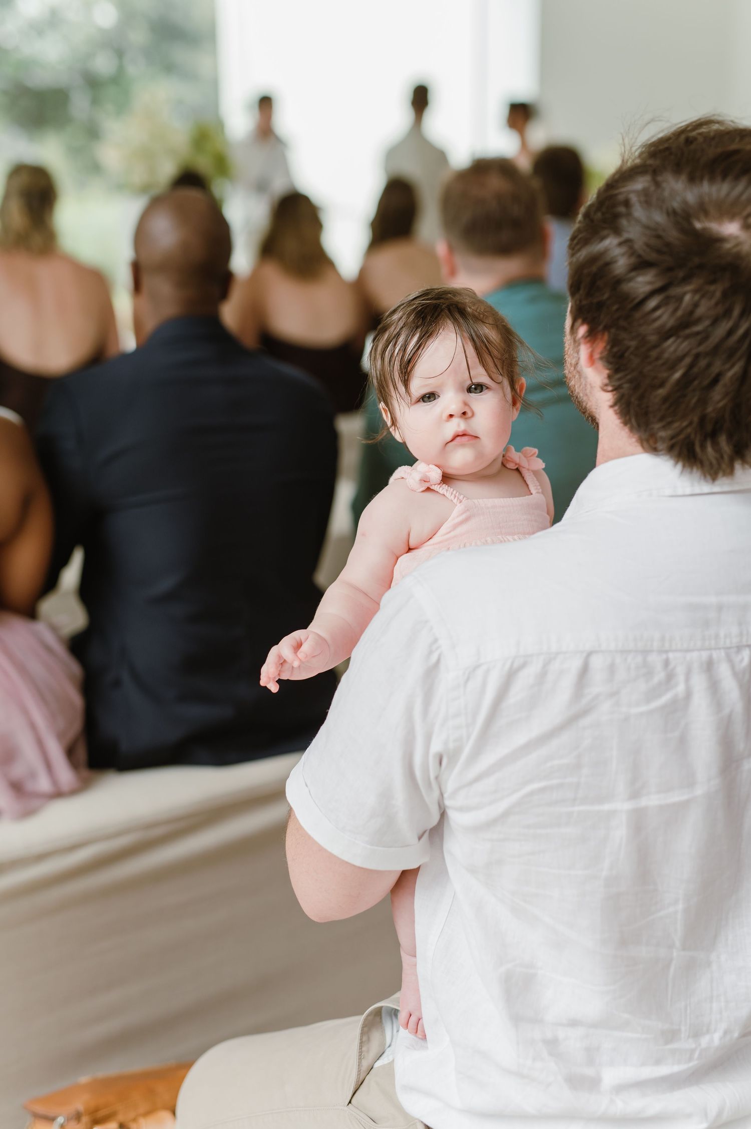 Small child in pink dress being held during wedding ceremony.