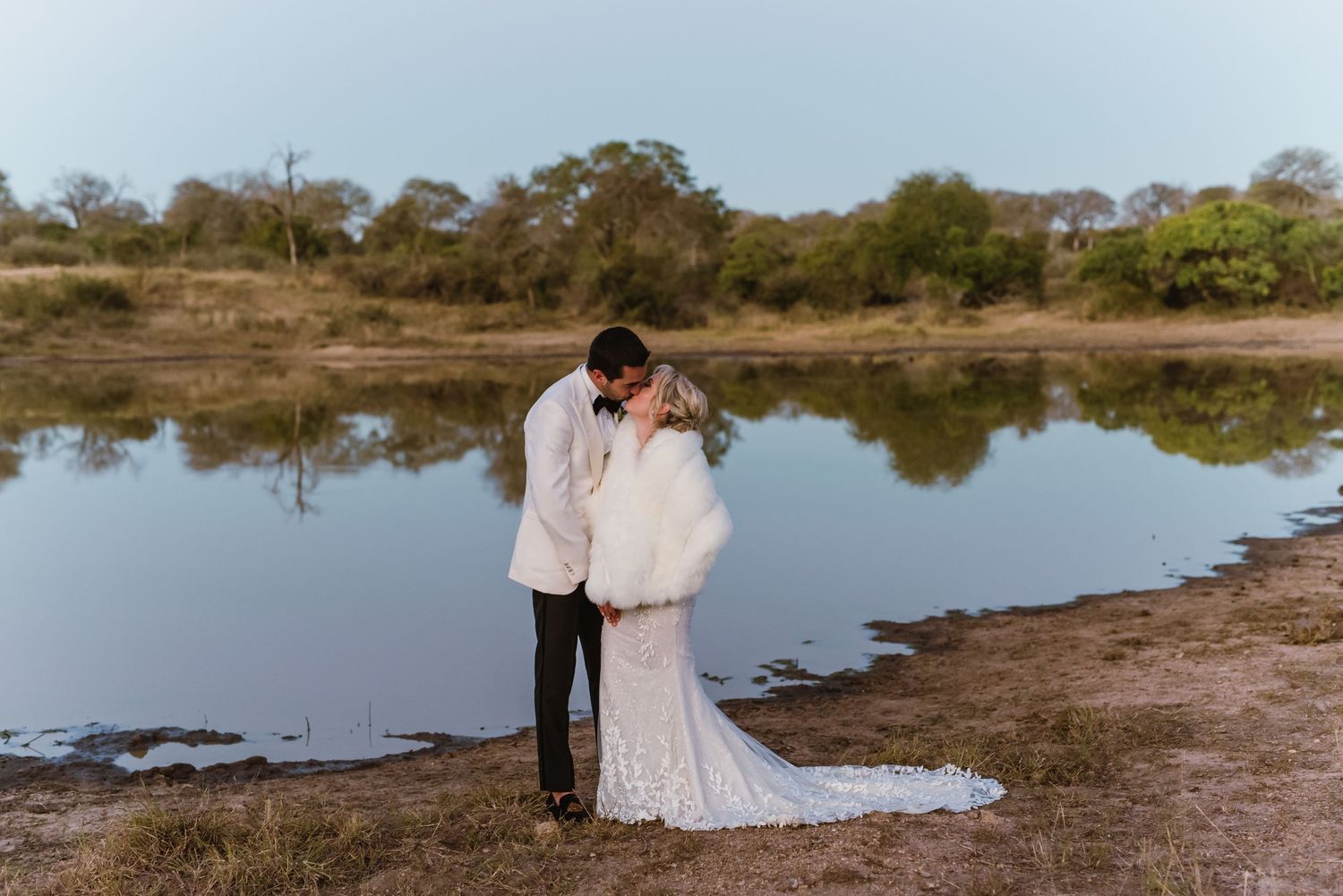 Newlyweds stroll beside a tranquil coastal lagoon at dusk.
