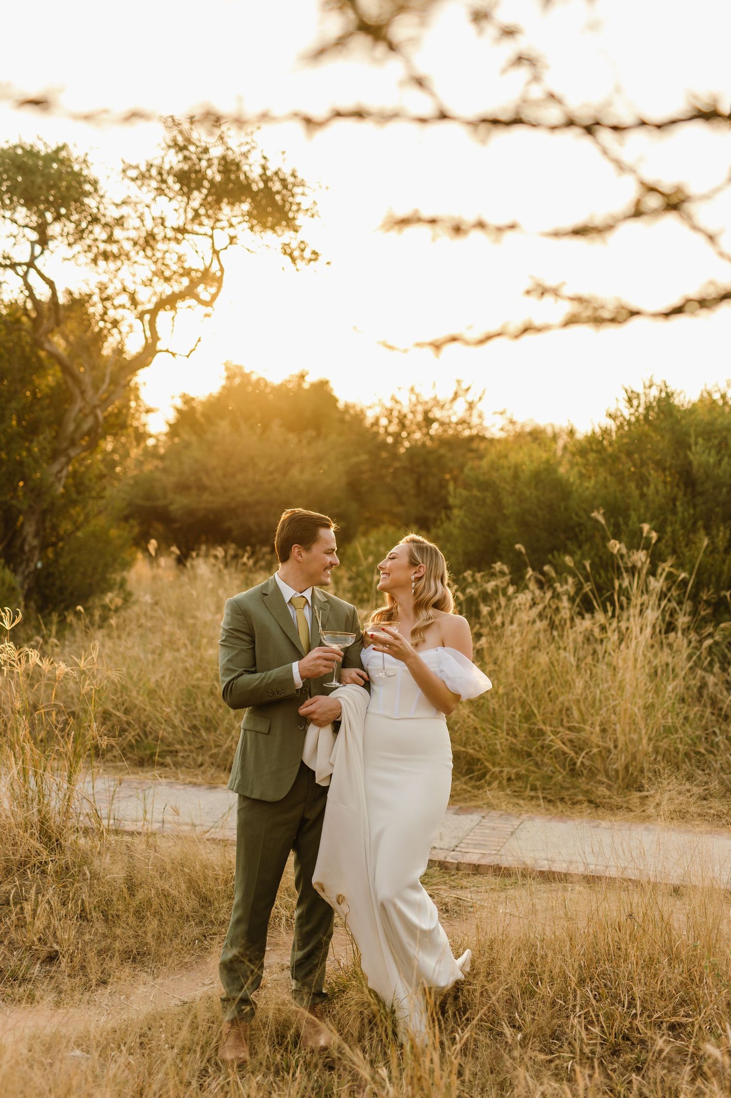 A romantic couple dances together on a dirt path during golden hour surrounded by tall grass.