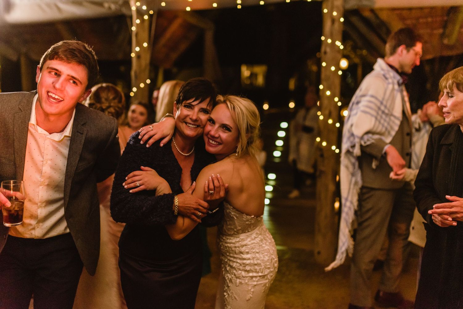 Wedding guests dancing and celebrating at an evening reception with twinkle lights overhead.