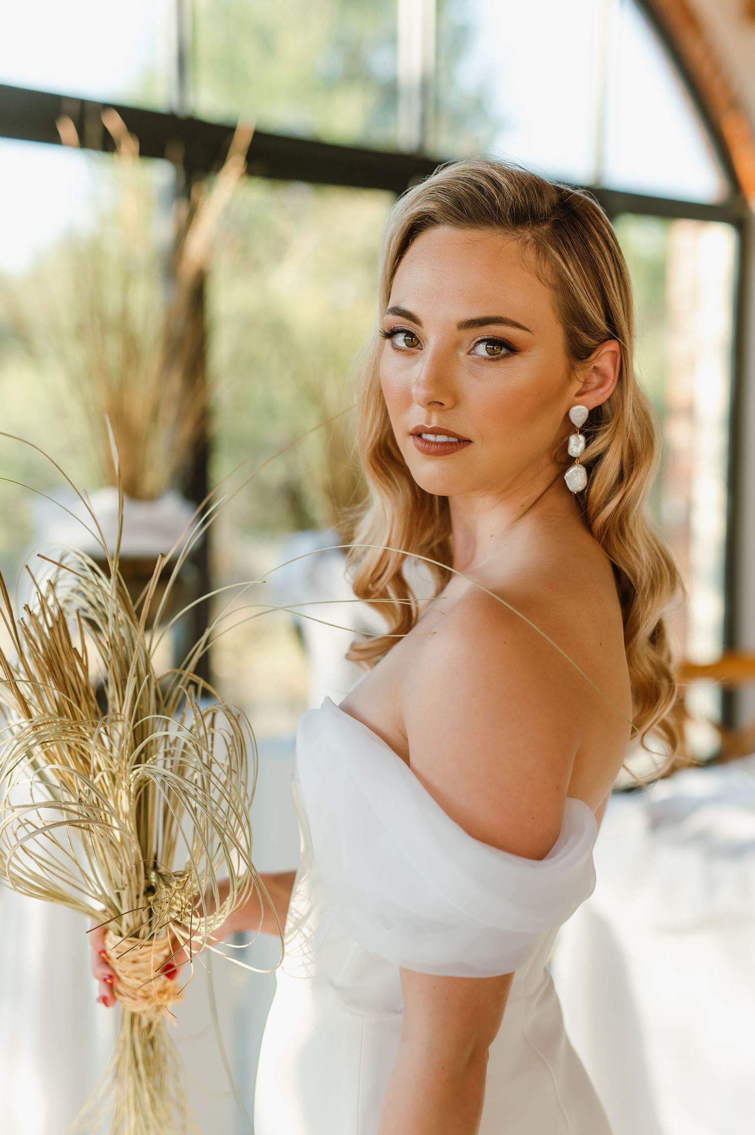 Bridal fashion details featuring an off-shoulder white gown and dried floral accents.