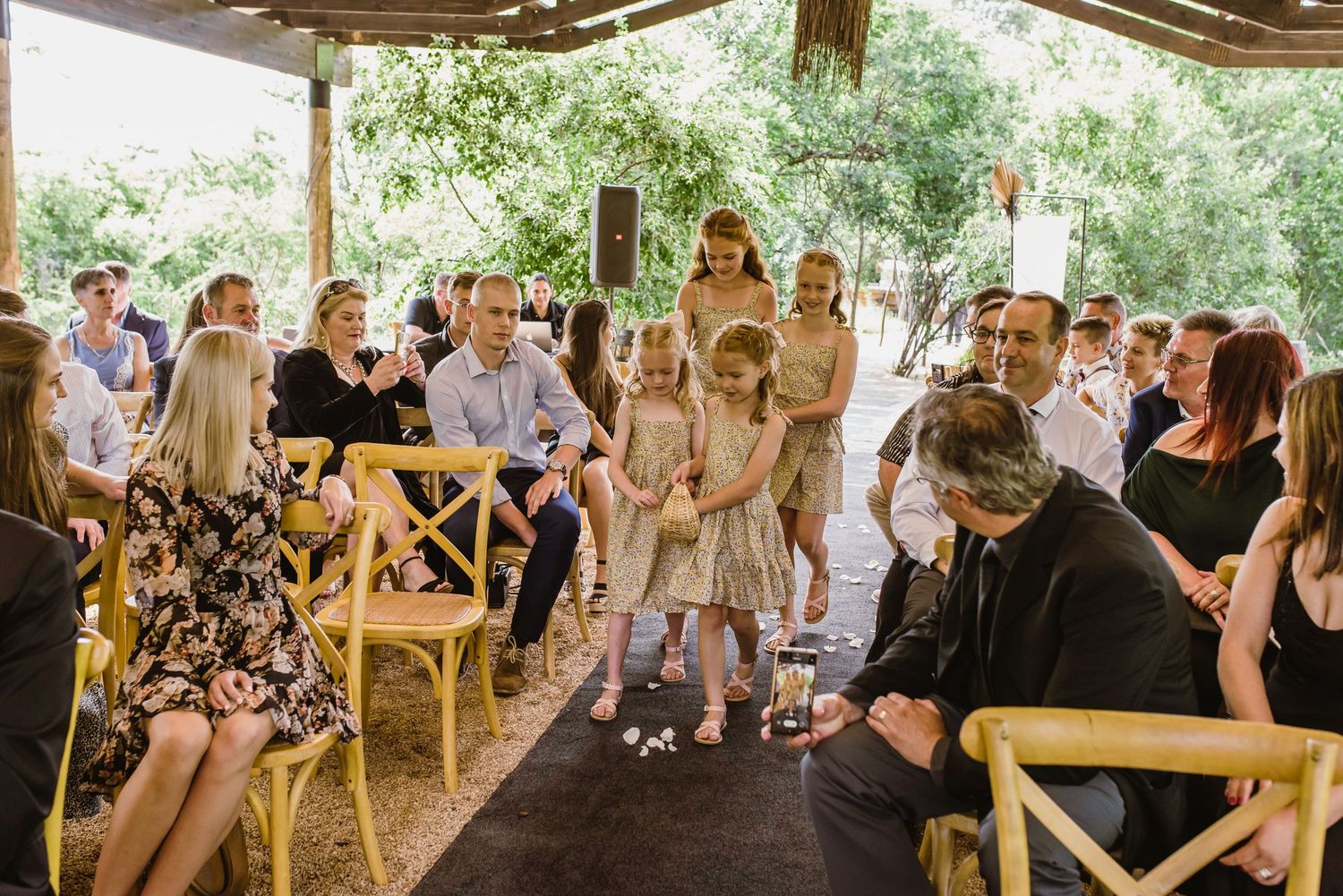 Wide view of wedding guests gathered under a covered outdoor pavilion for a ceremony.