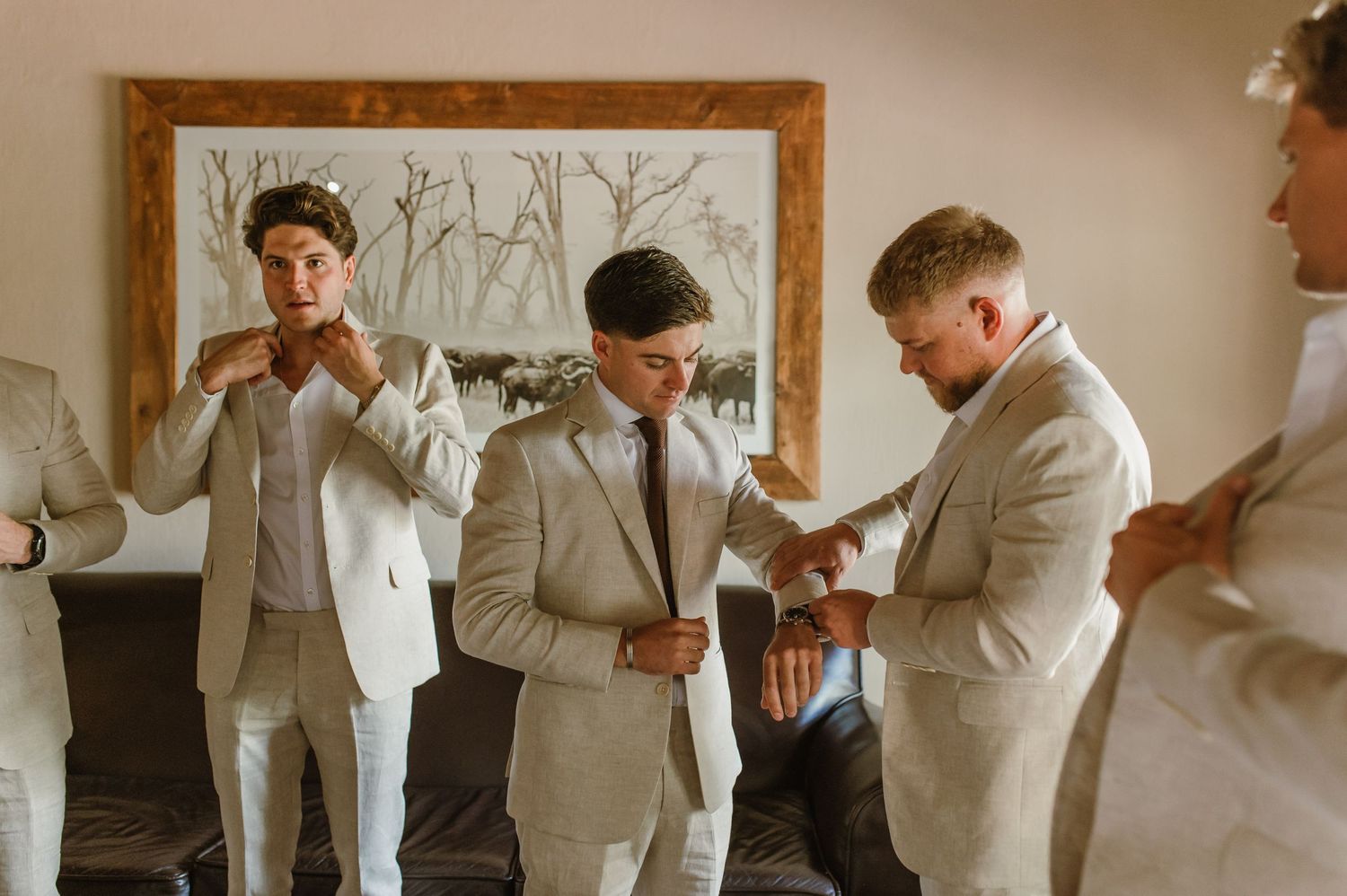 Groomsmen in light colored suits share emotional moments while getting ready for a wedding.