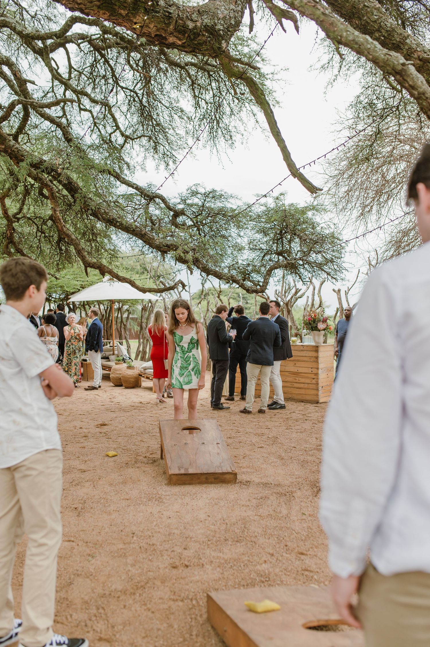 Outdoor wedding reception venue with guests mingling under large trees and white tents.
