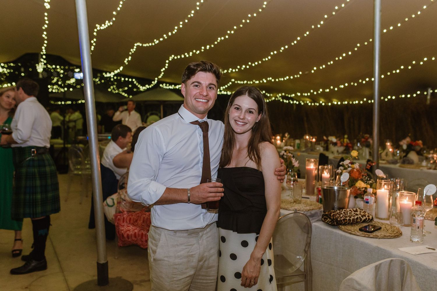 Wedding reception venue with elegant table settings and string lights creating romantic ambiance.