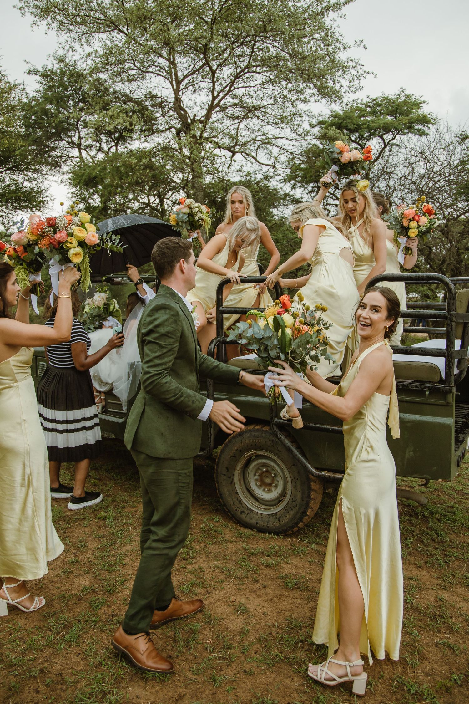 Wedding party celebrates with joyful dancing near vintage vehicles at outdoor reception.