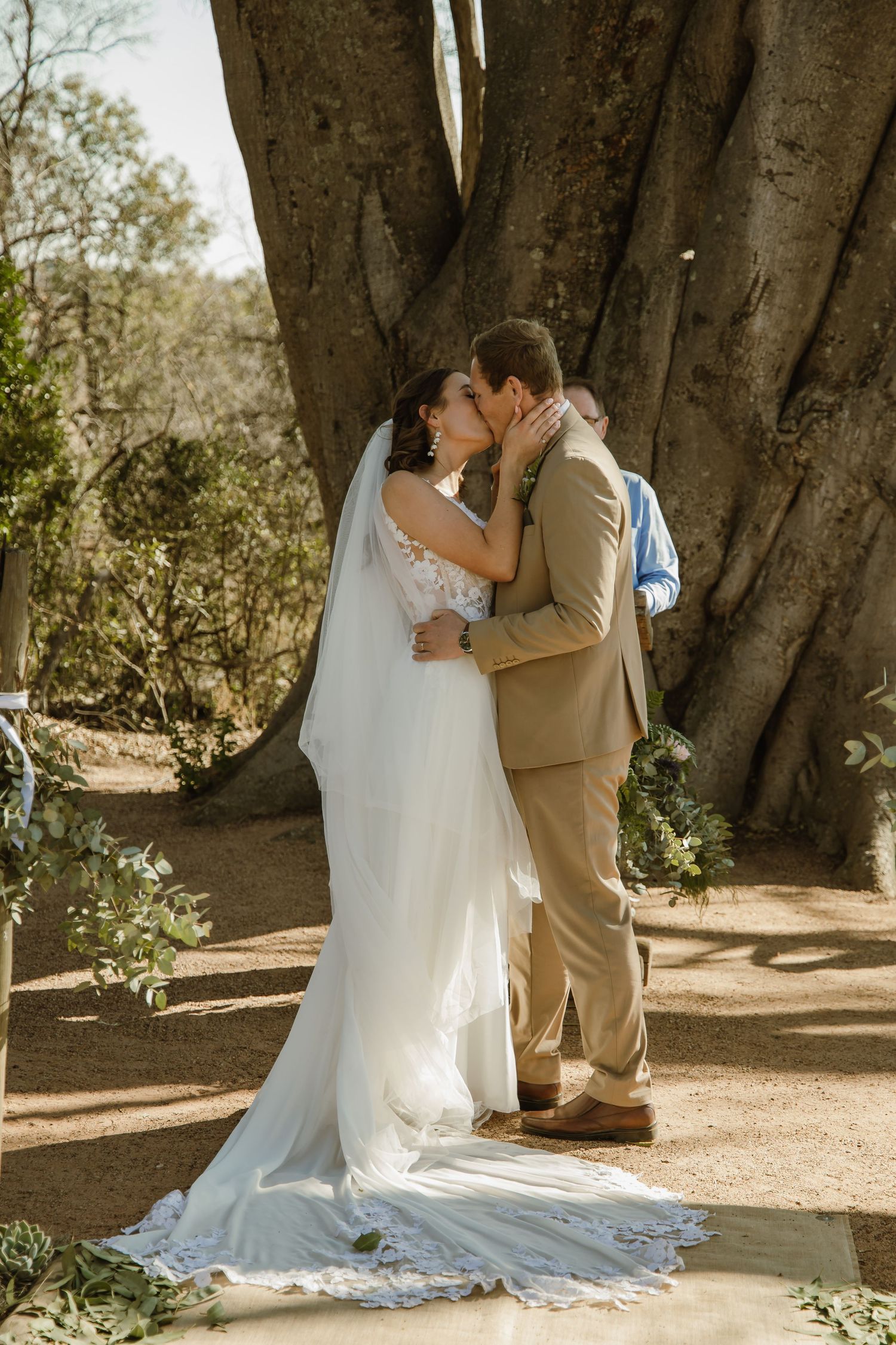 Intimate wedding moments captured under a large desert tree during the ceremony.