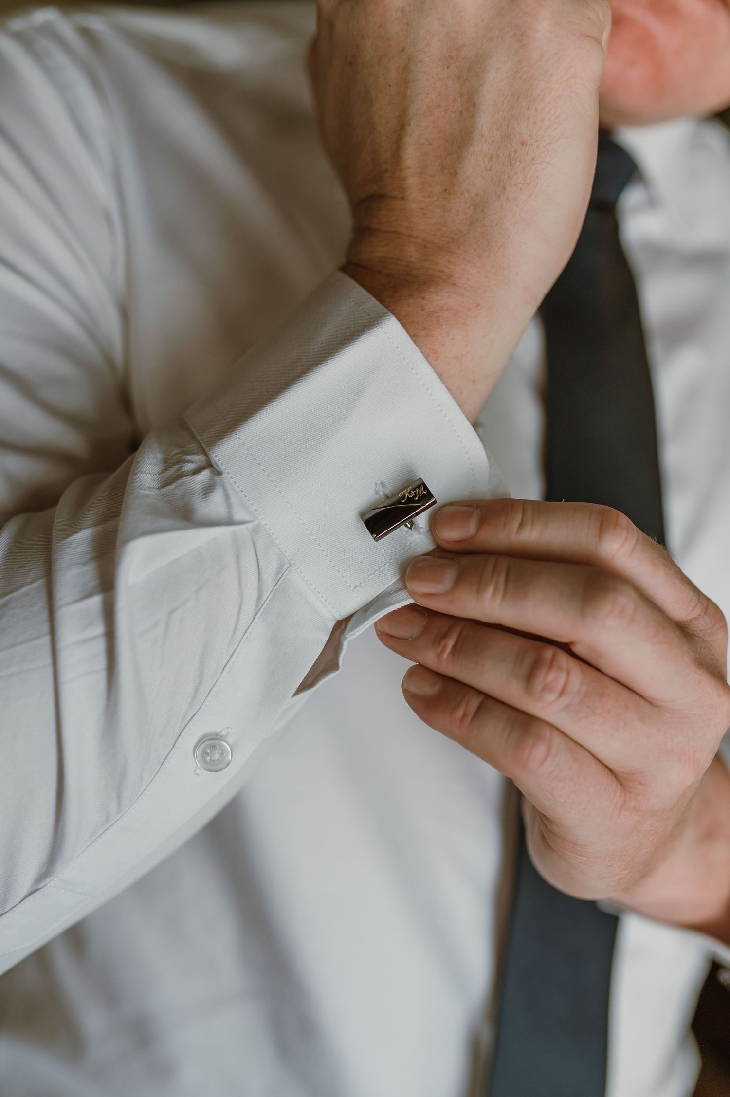 Close-up shots of hands fastening cufflinks on a white dress shirt sleeve.