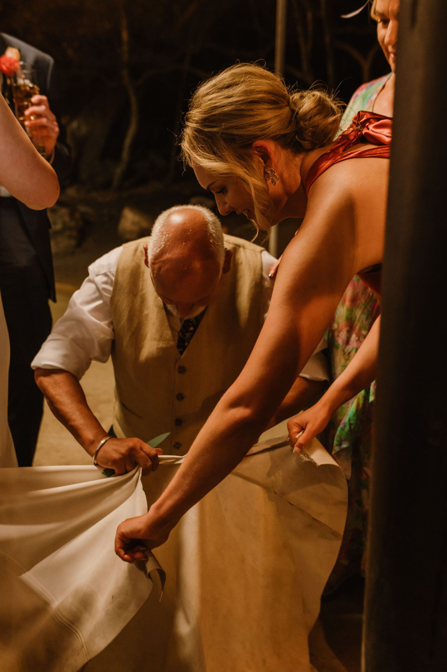 Wedding guests assist with dress arrangements during reception festivities.