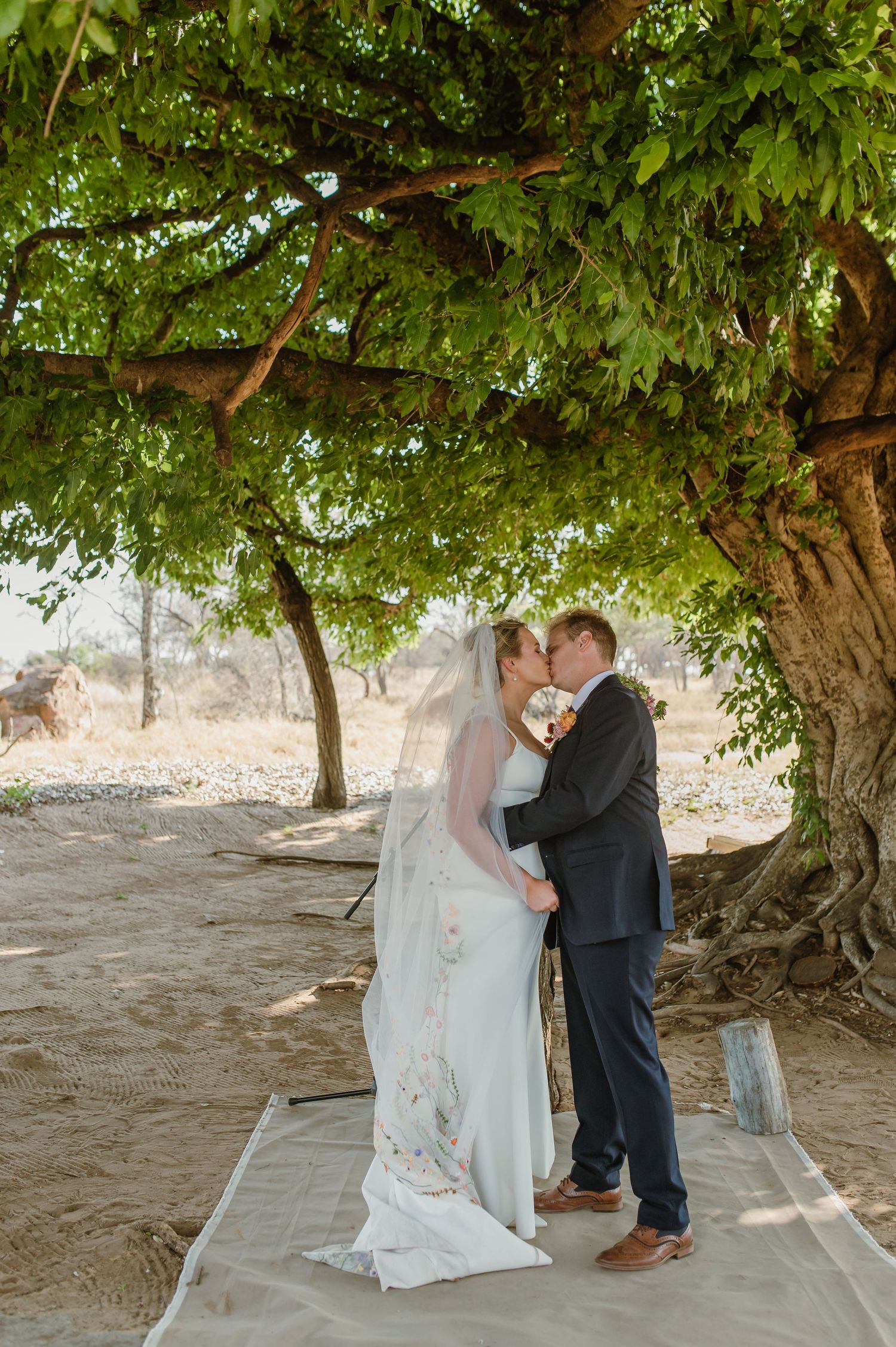Couple shares intimate moment during wedding ceremony under tree canopy.