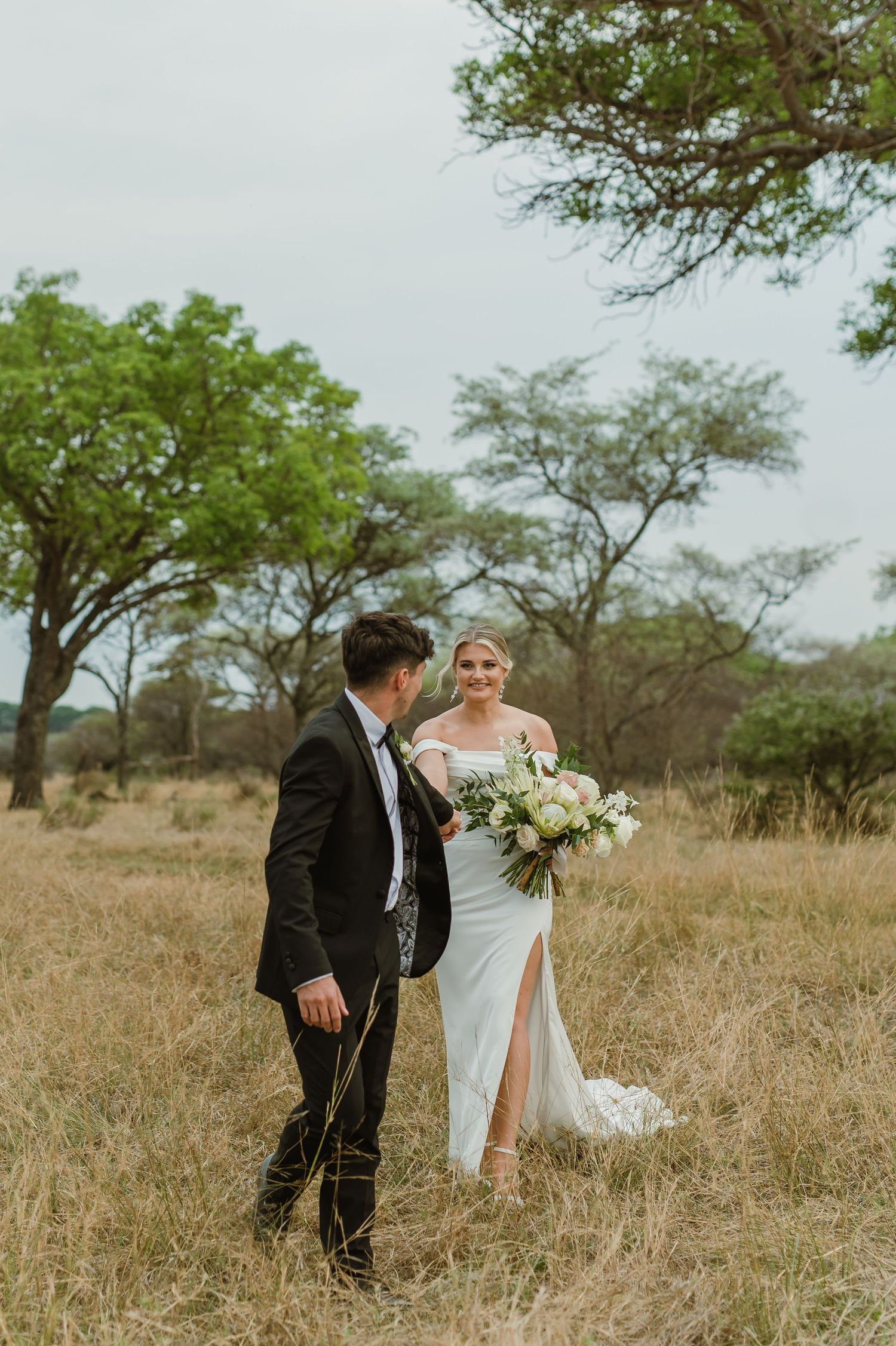 Wedding couple shares intimate moment in a golden field with scattered trees.