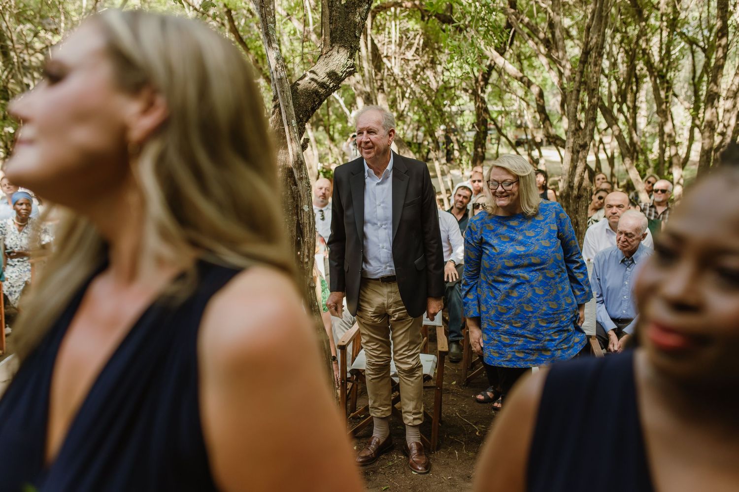 Wedding party stands in a lush forest setting during an outdoor ceremony.