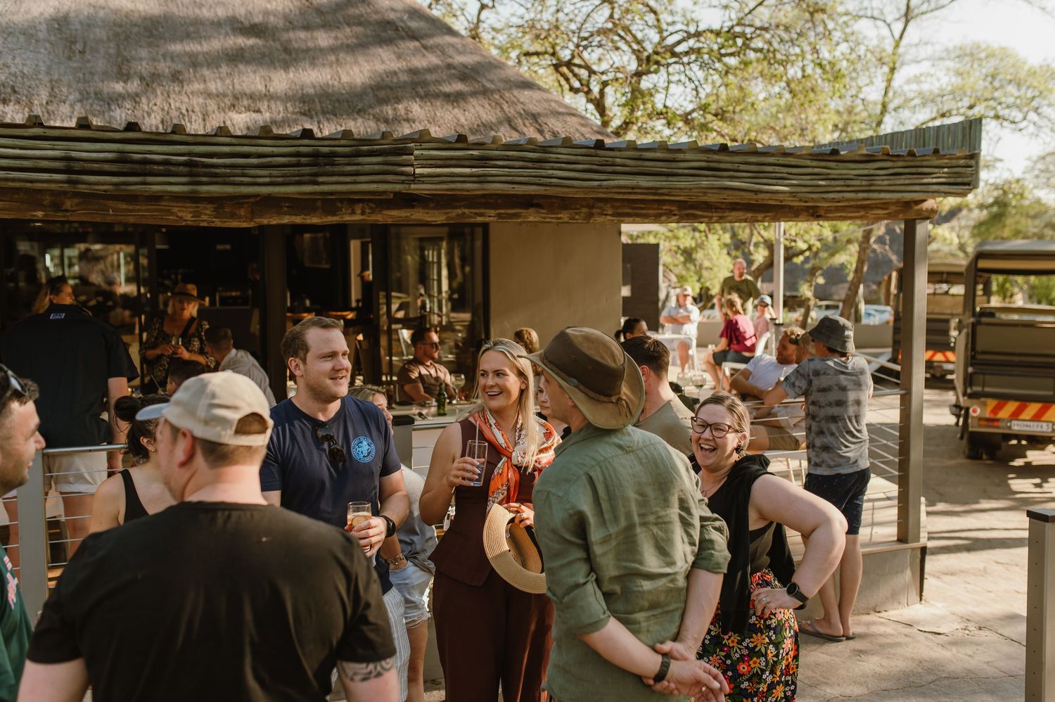 Exterior view of a safari lodge with guests gathering under thatched roofs.