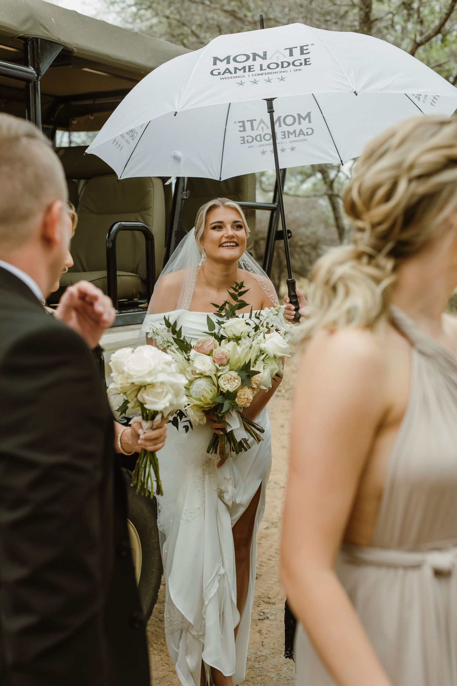 Wedding party holds white umbrellas while posing with elegant bouquets in an outdoor setting.