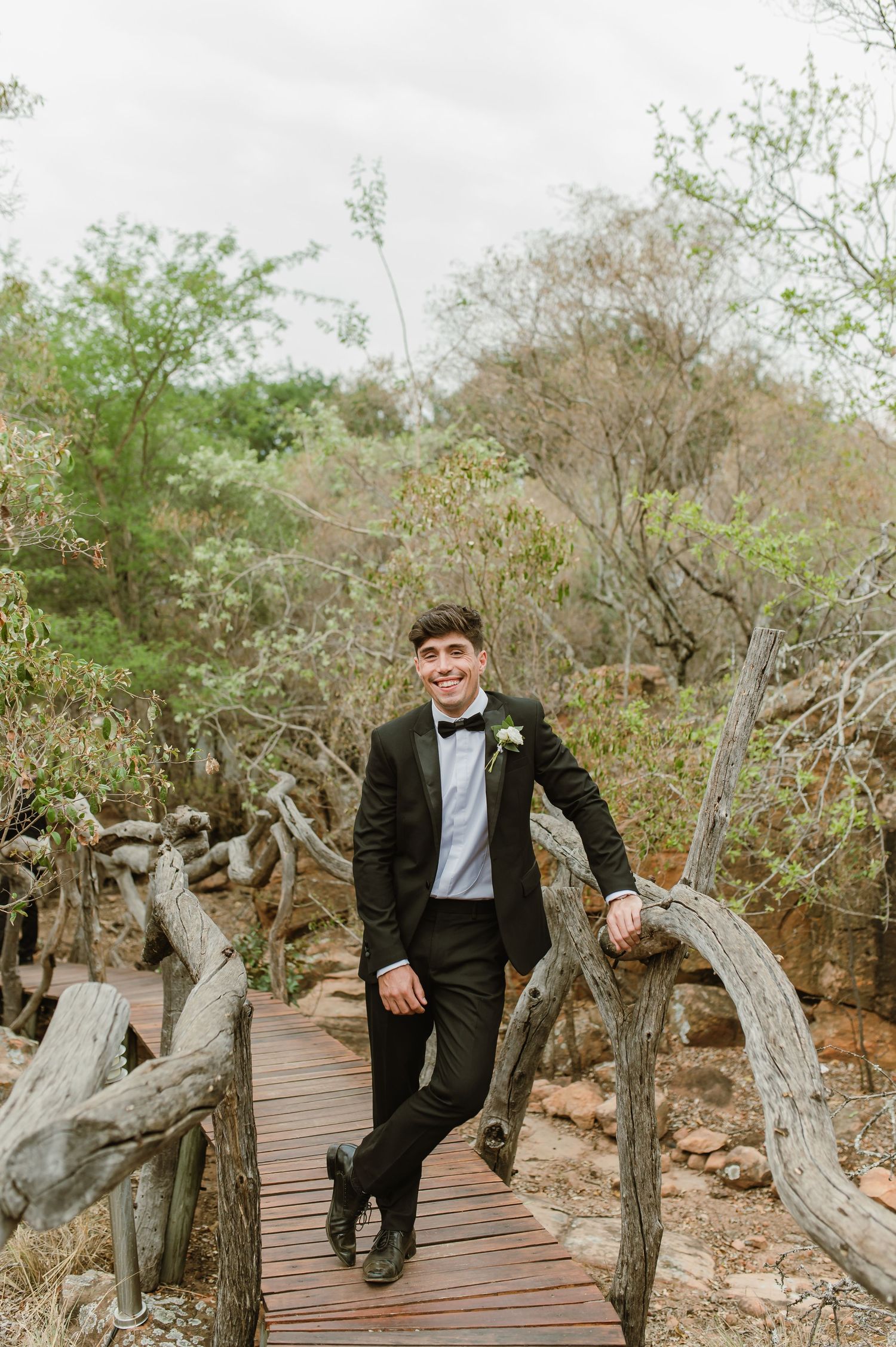 Groomsmen walk along a wooden boardwalk surrounded by desert brush and rocks.