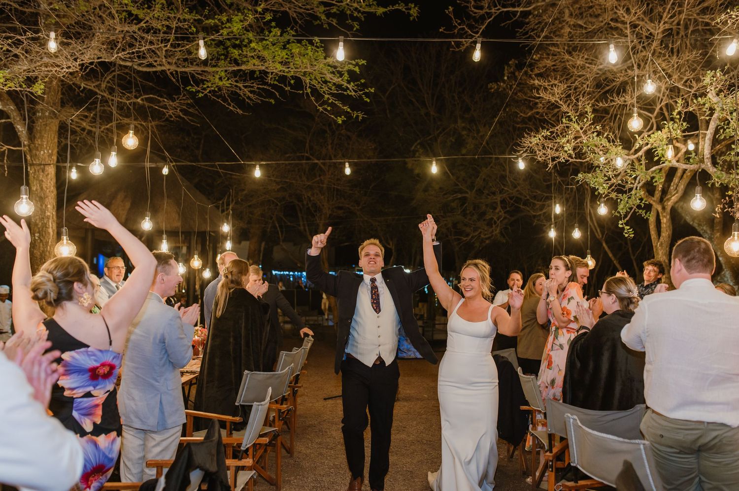 People dancing and celebrating at an outdoor evening event under string lights.