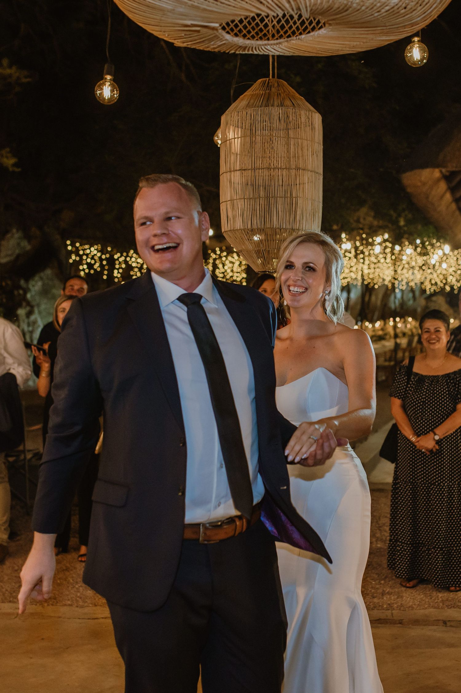 Wedding couple shares a joyful dance moment under rustic rattan pendant lights at an outdoor evening reception.