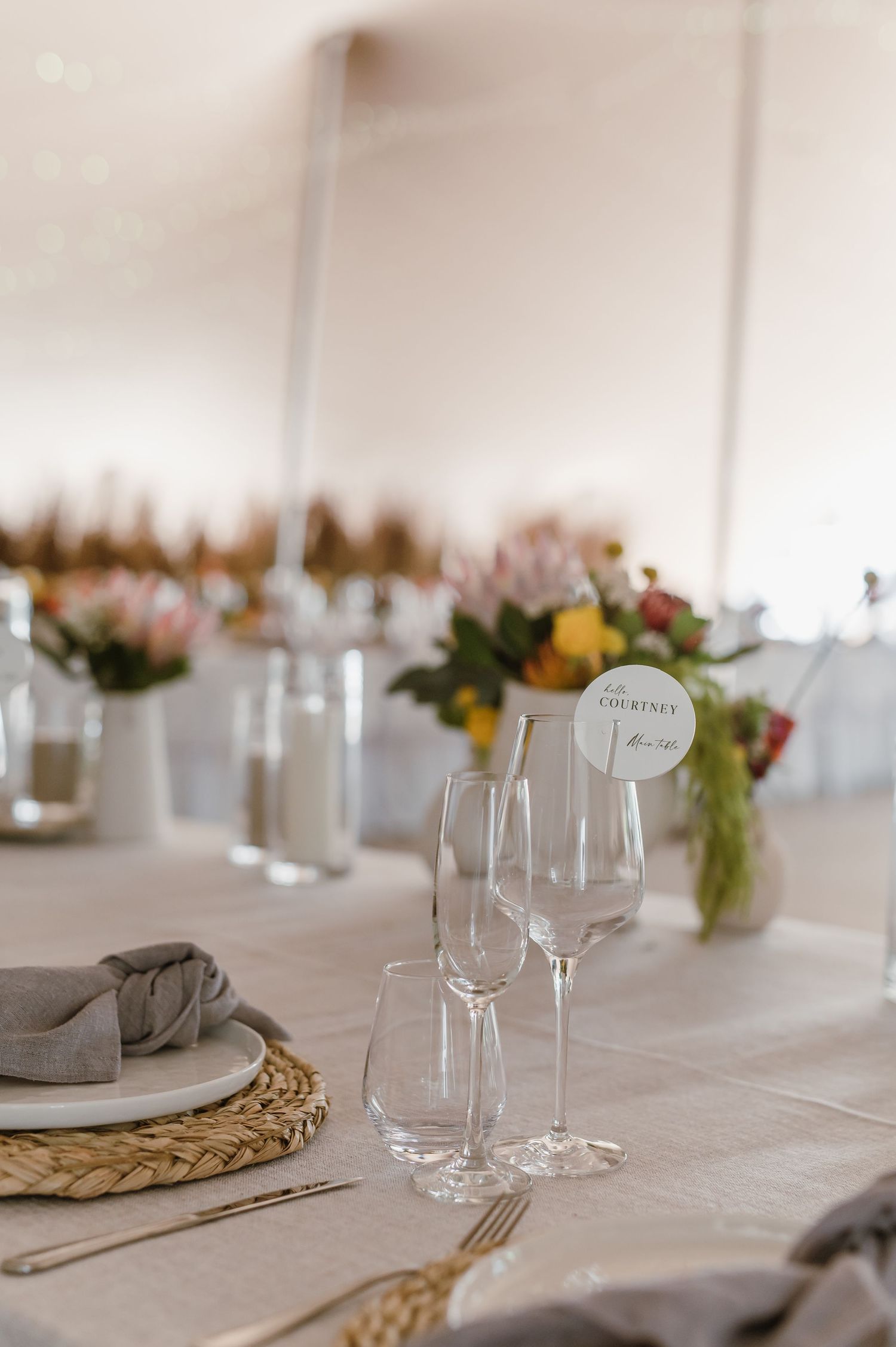Wedding reception table settings with natural woven placemats and soft gray napkins.