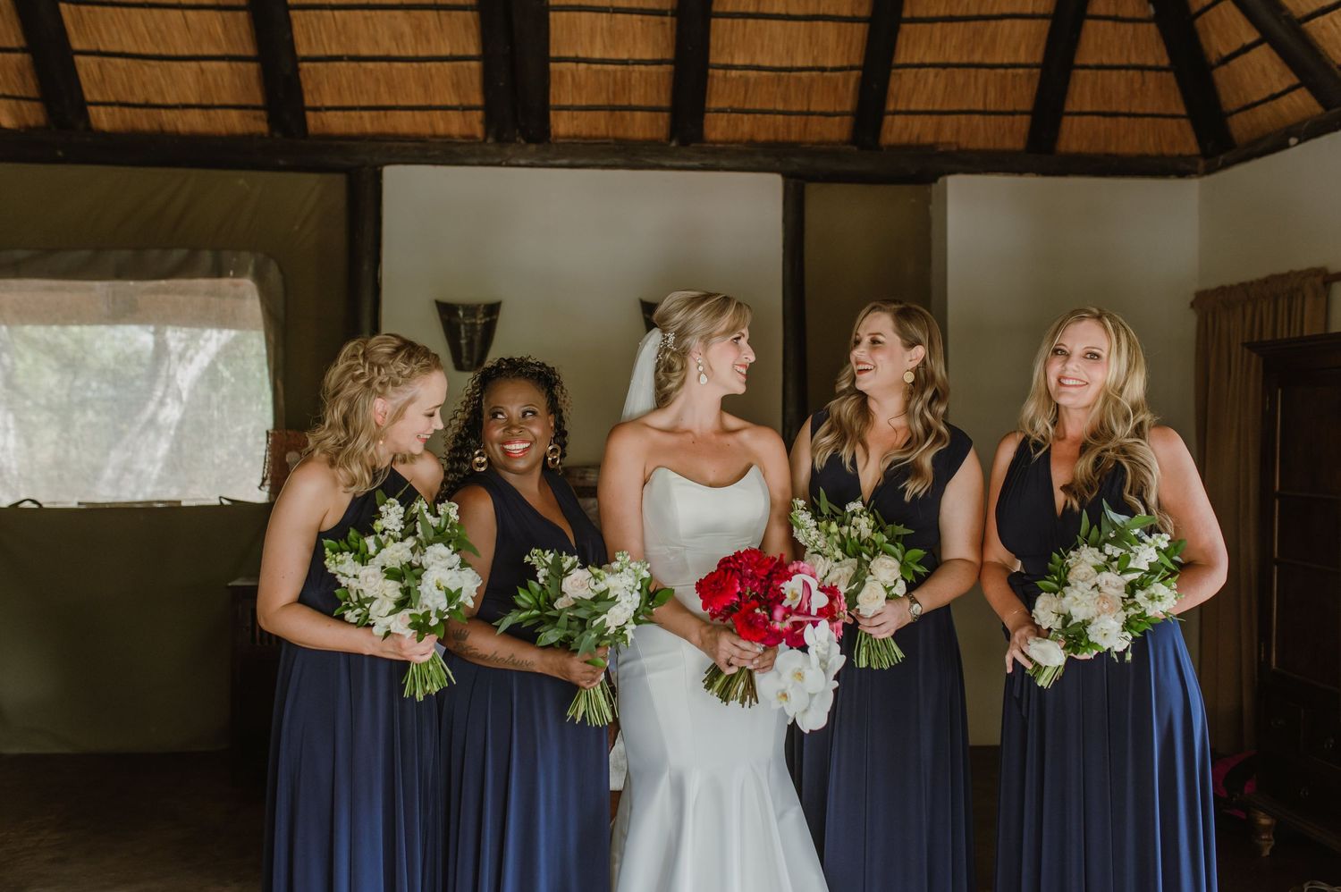 Wedding party in navy blue dresses holding bouquets outdoors.
