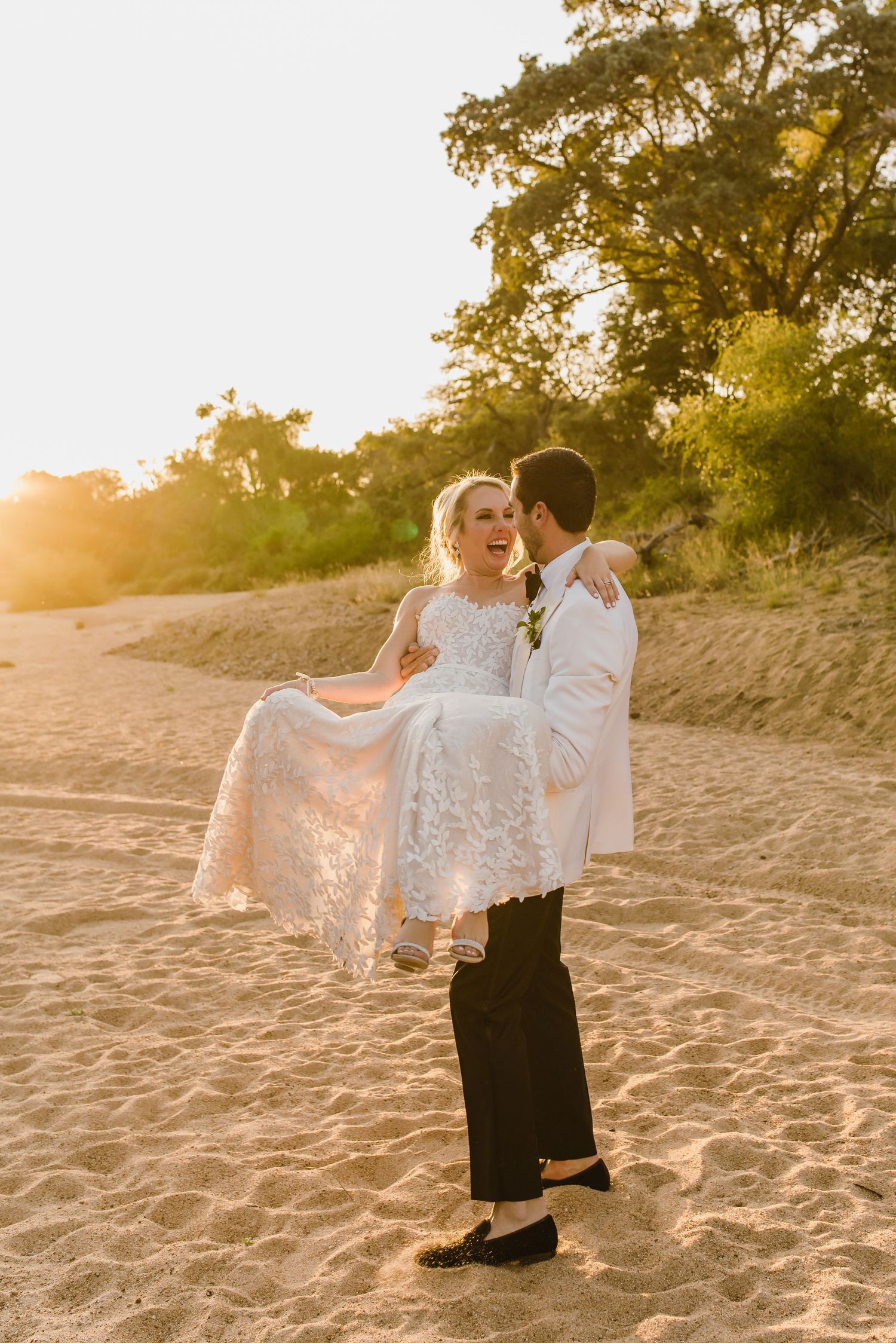 A romantic couple dances on a sandy beach at sunset with sunlight filtering through trees creating a golden glow.