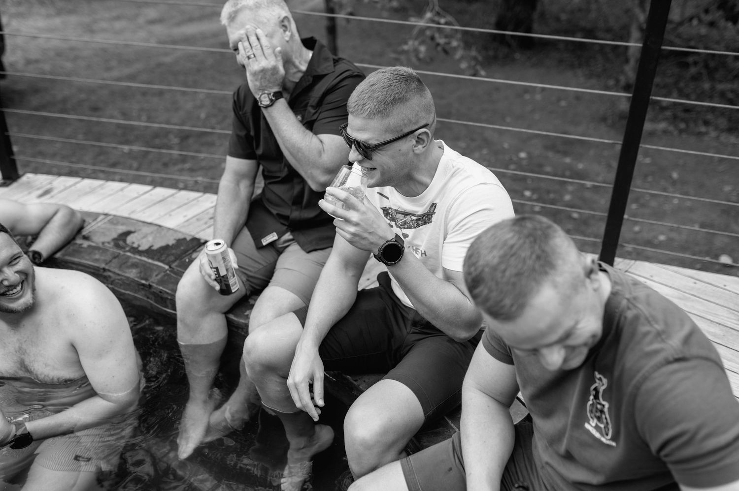 Black and white photo of groomsmen relaxing outdoors on wooden steps before a wedding ceremony.