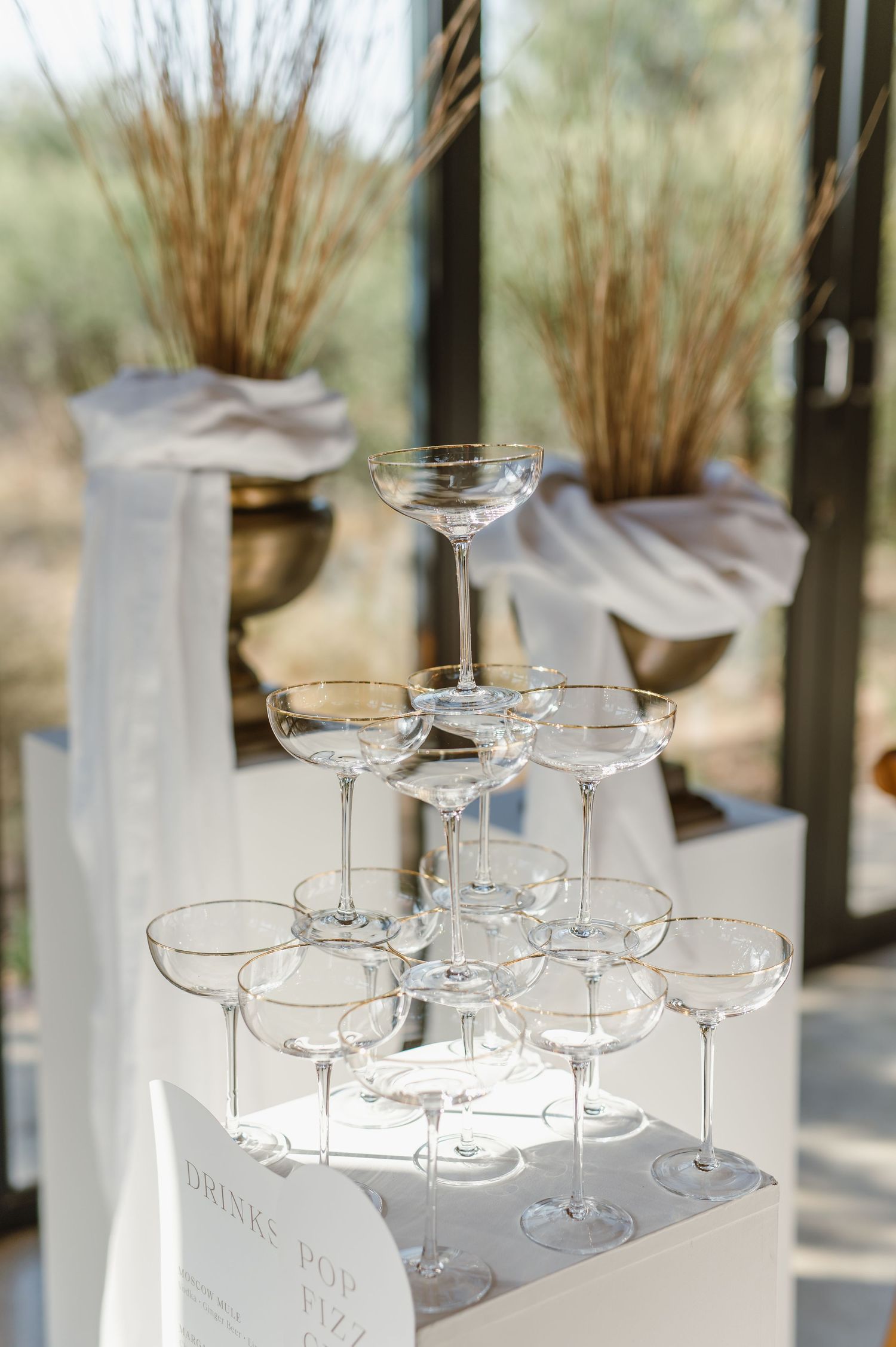 Champagne tower display with coupe glasses arranged in elegant tiers near window light.
