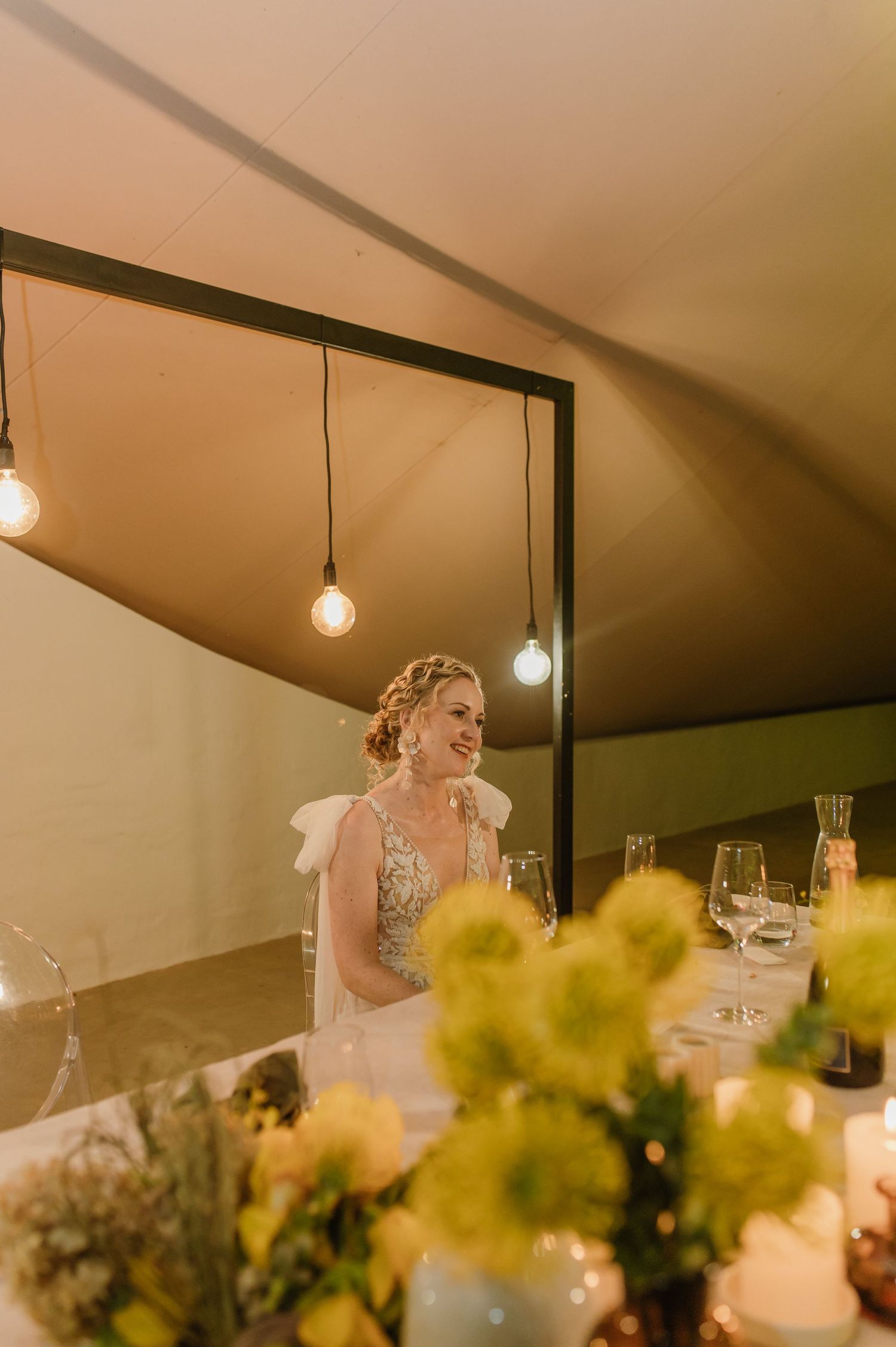 Wedding reception table decor with hanging lights and yellow floral arrangements.