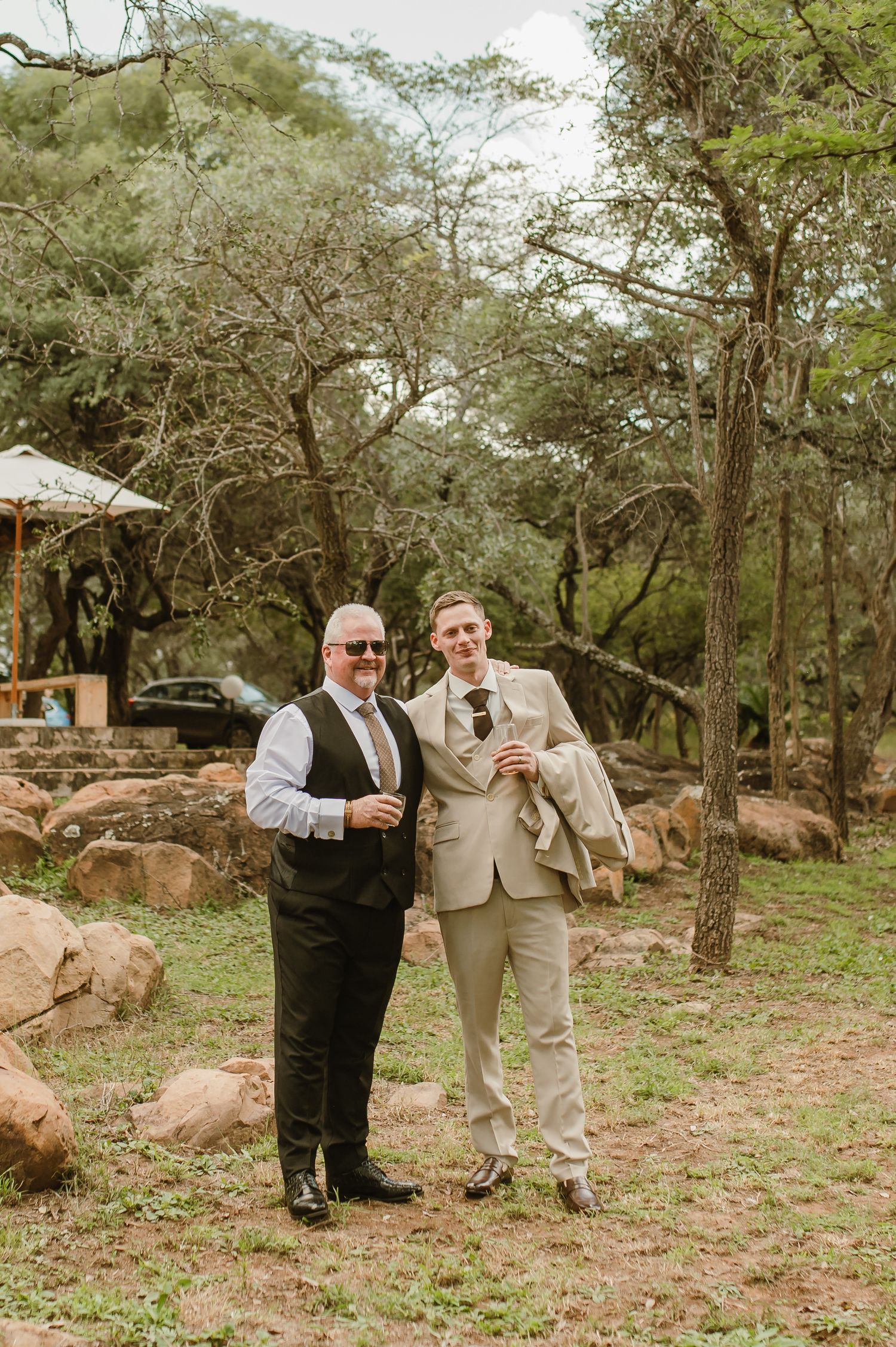 Two people in formal attire standing together in rocky outdoor landscape.