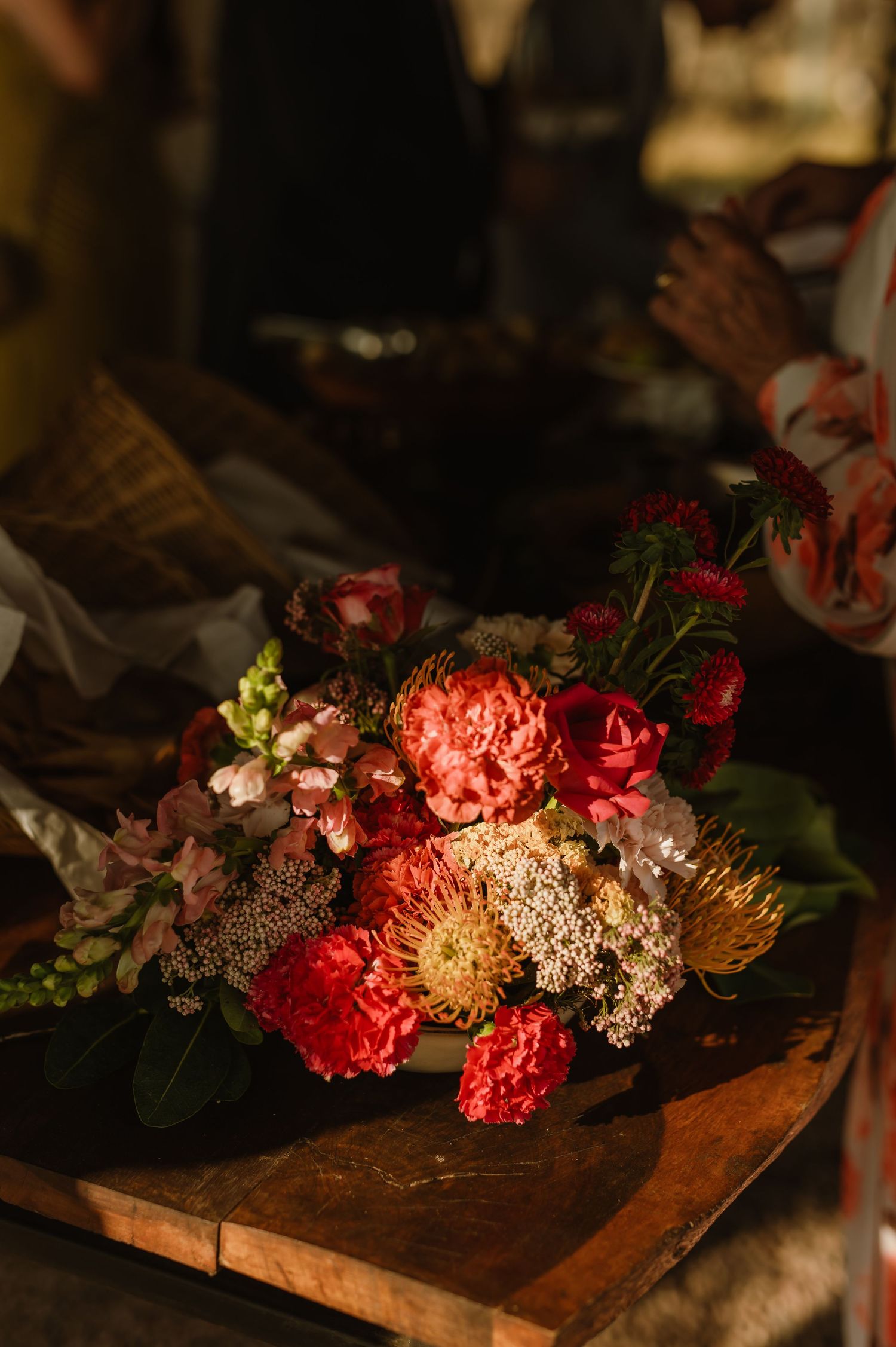 Moody floral arrangement with pink and coral blooms on wooden surface.