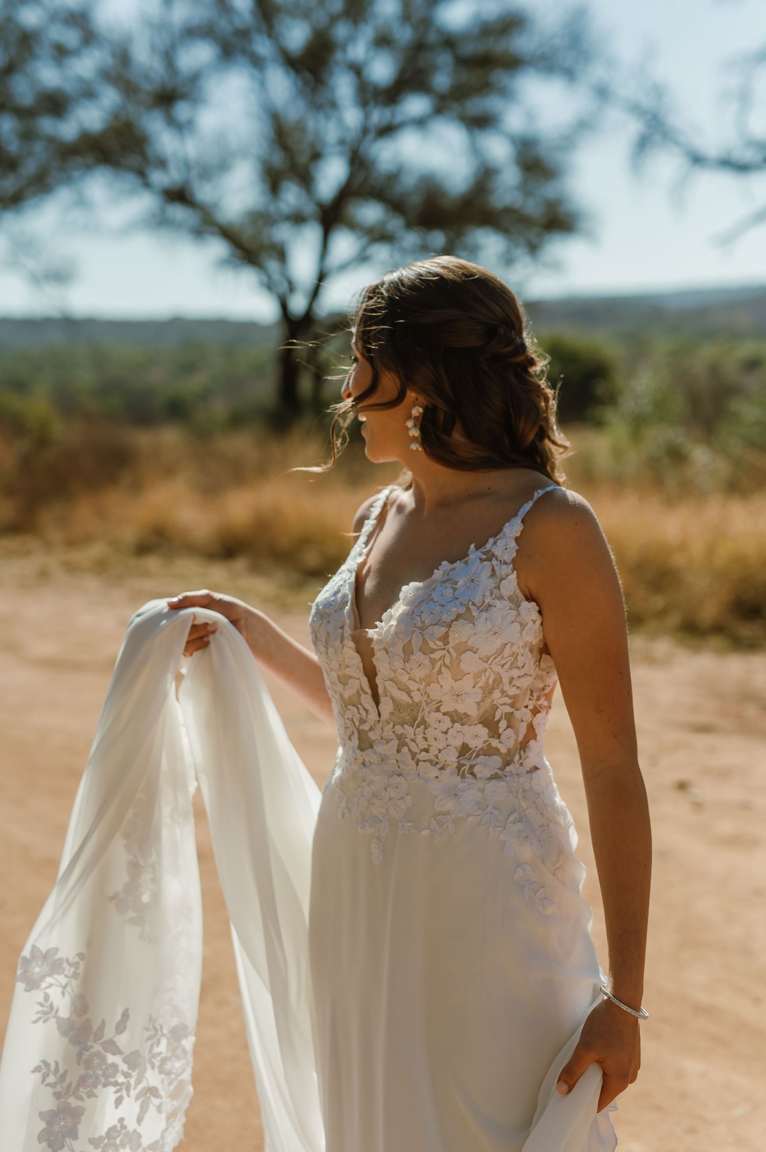 Back view of bride in detailed lace wedding dress with flowing veil in desert setting.