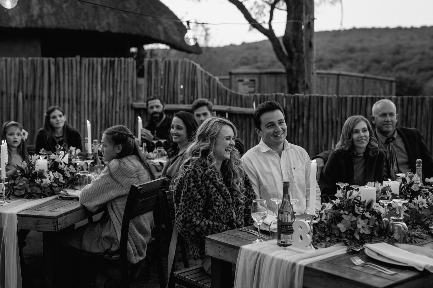 Intimate outdoor dining setup with wooden tables and rustic decor under a bamboo fence enclosure.