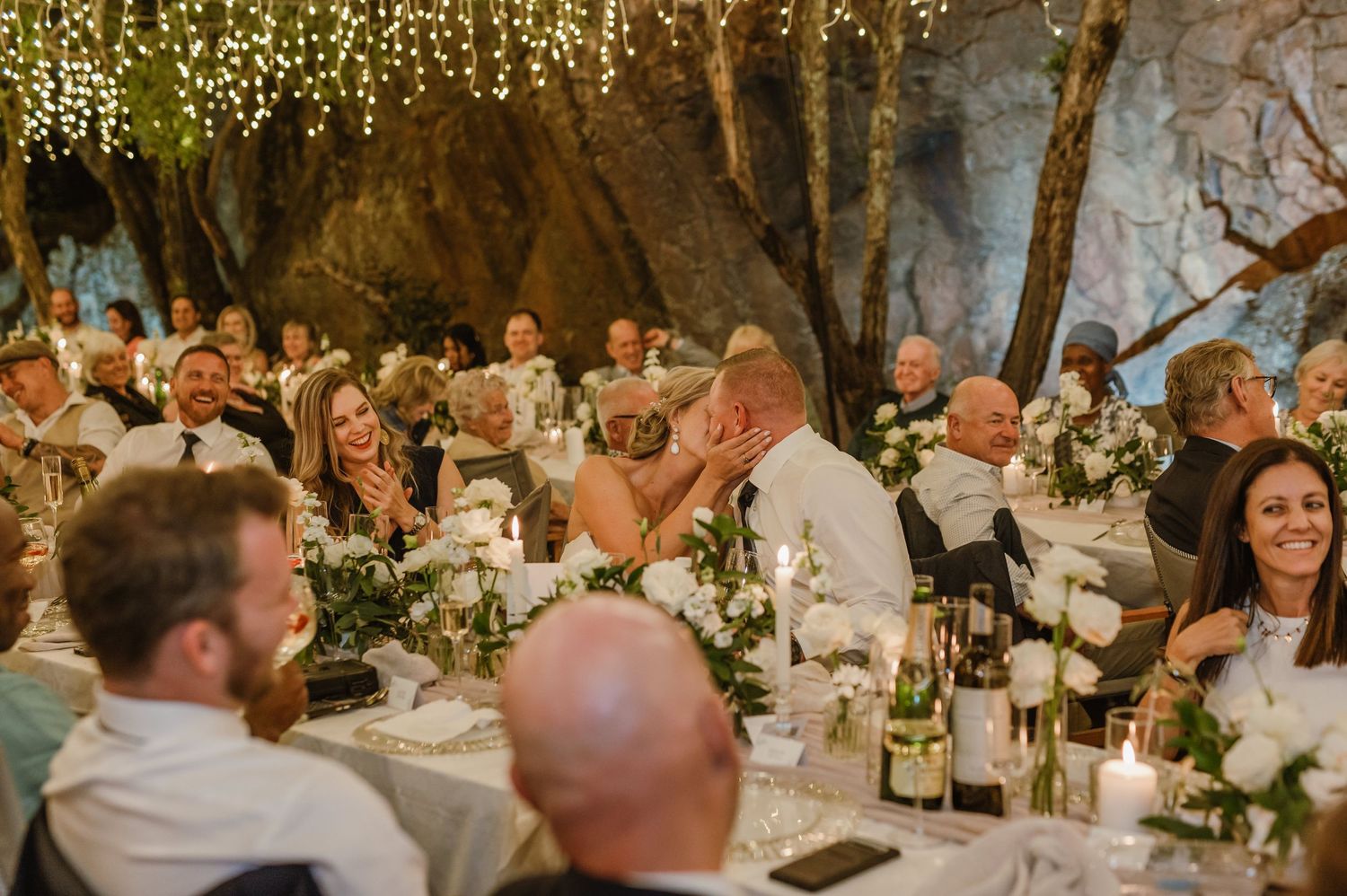 Guests celebrating at an intimate wedding reception under warm fairy light decorations.