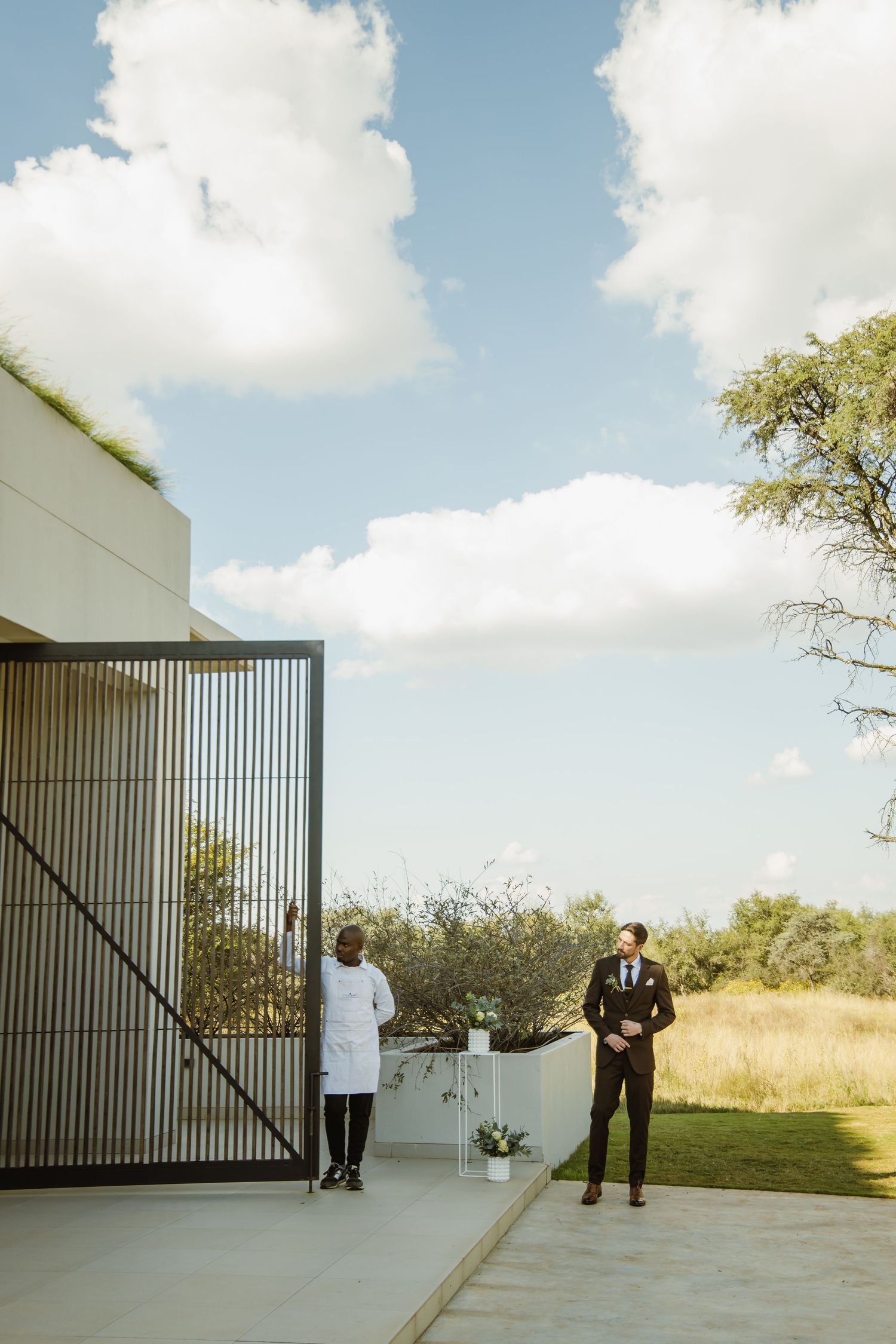 Modern minimalist wedding ceremony venue with white walls and vertical slat gate against a bright blue sky.