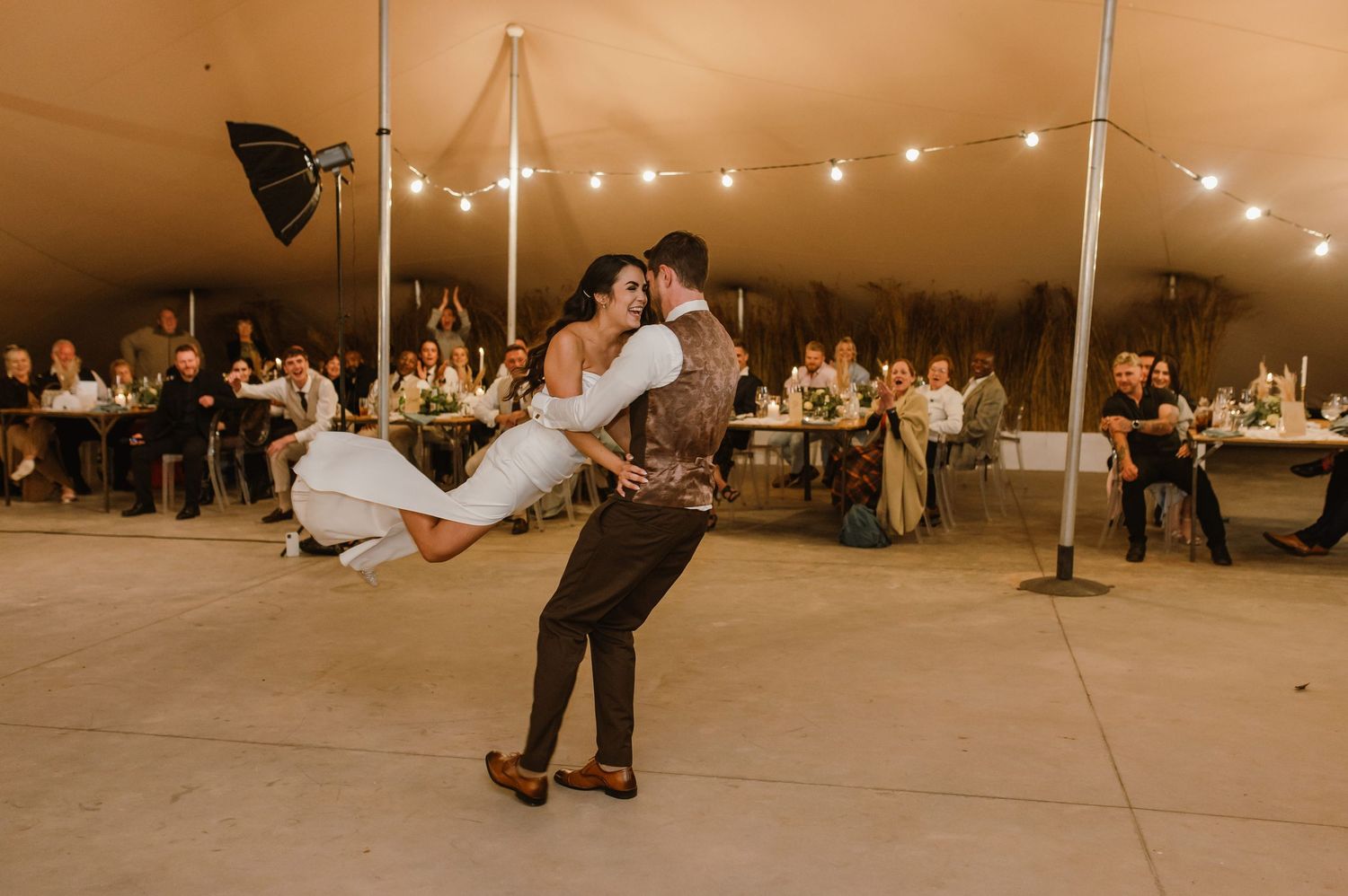 Wedding guests dancing and celebrating on tent dance floor with string light ambiance.