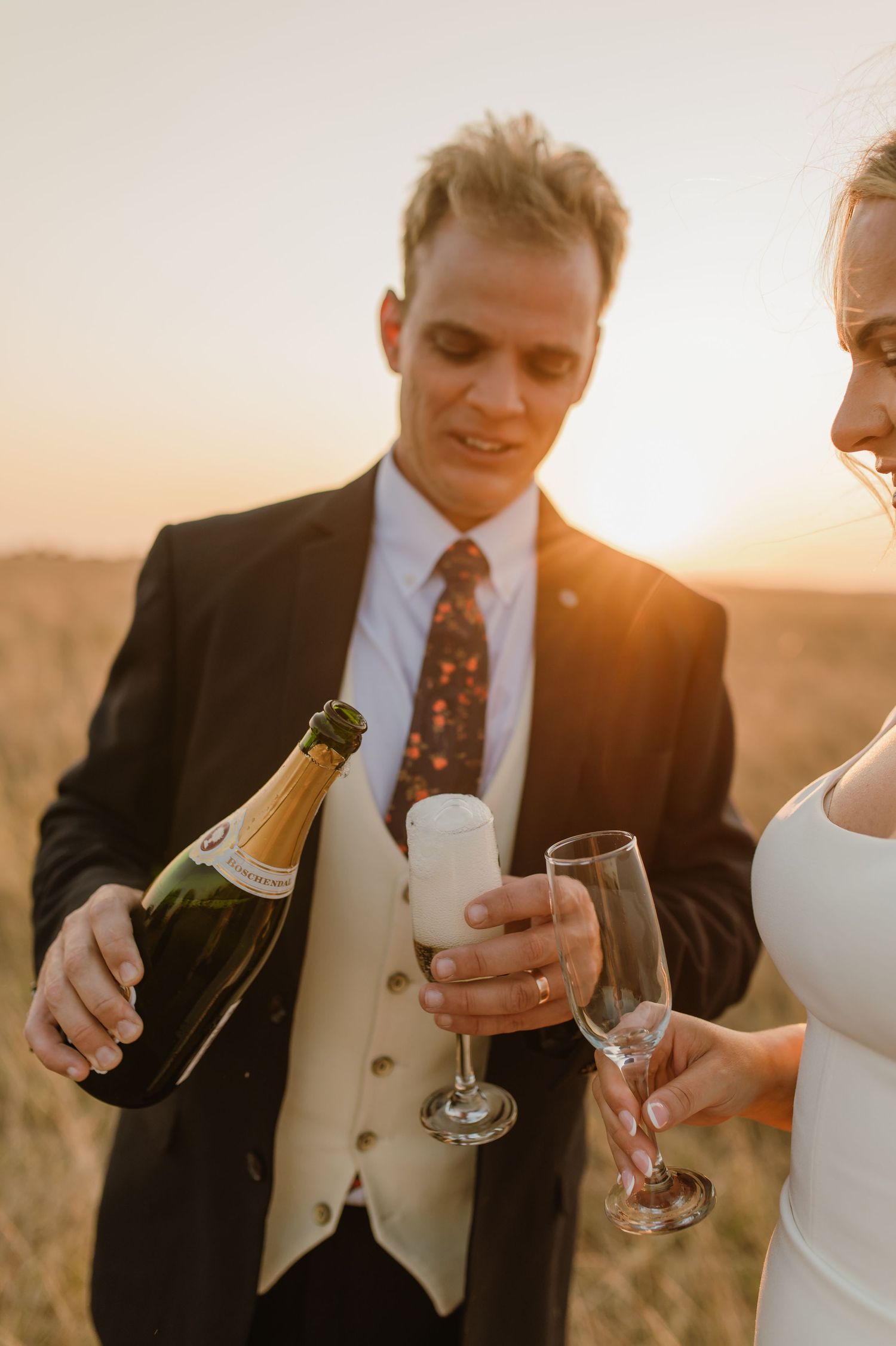 Couple pouring champagne into glasses during sunset wedding photoshoot.