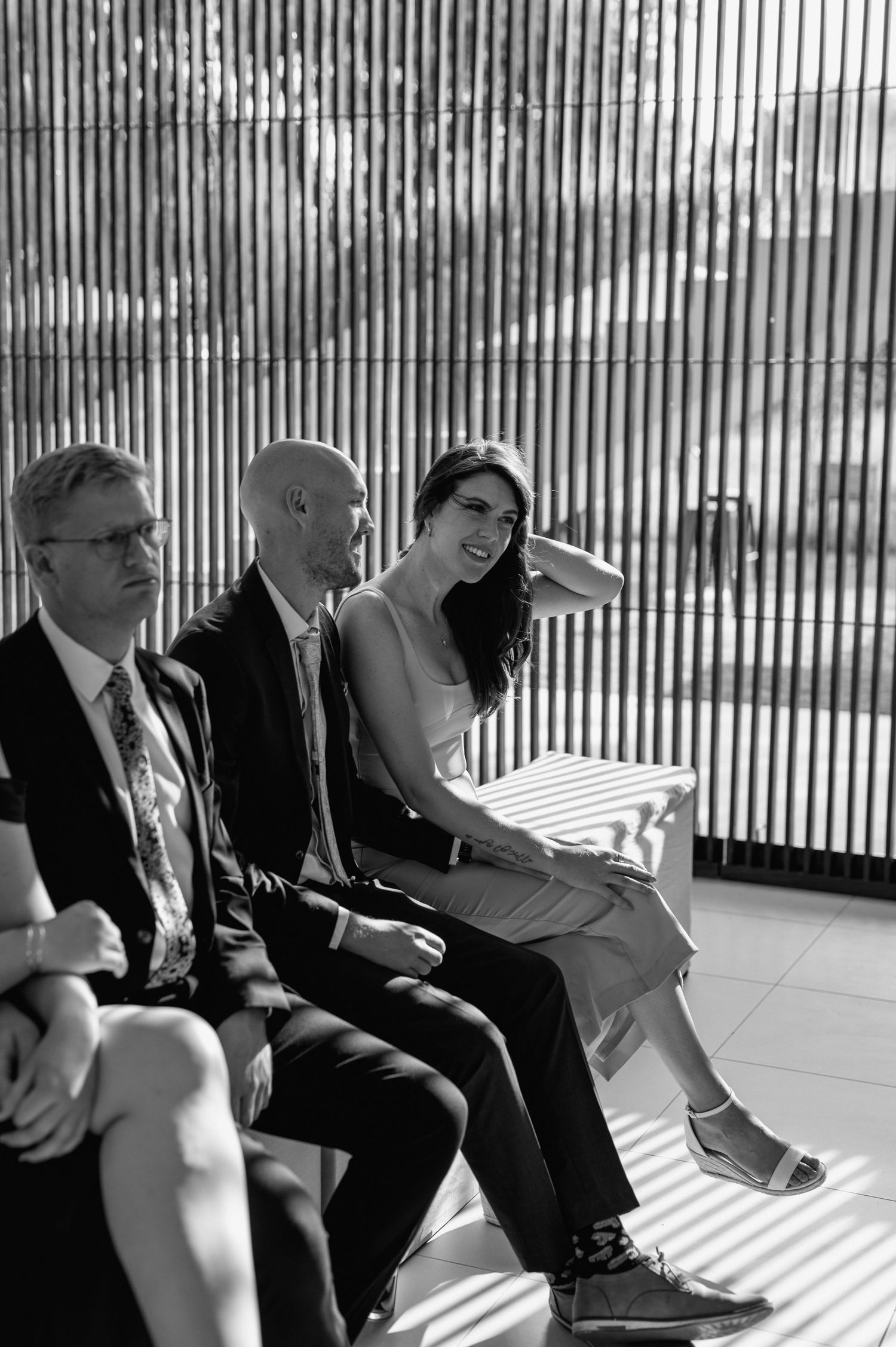 Black and white photo of wedding guests seated in a room with dramatic striped lighting.