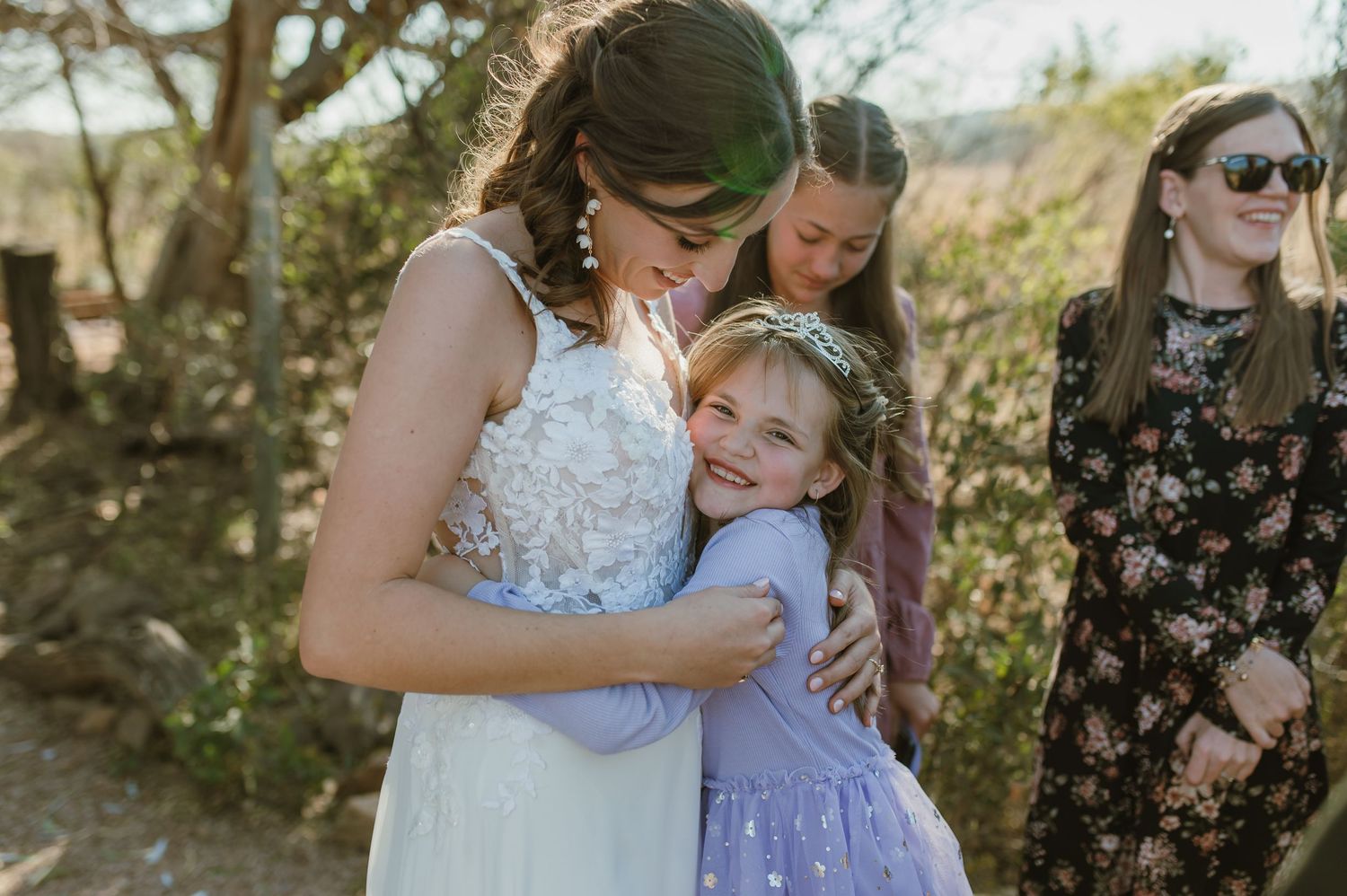 Guests in pastel dresses celebrate during a sunny outdoor wedding celebration.