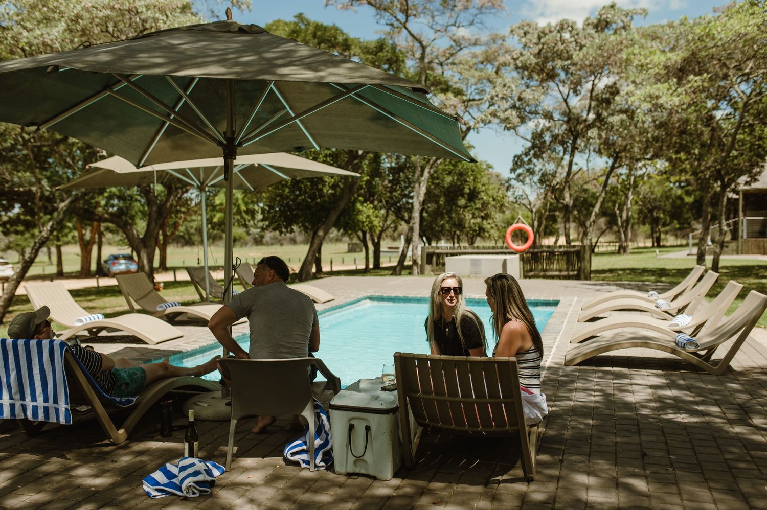 Guests relaxing by pool under large umbrella at safari resort.