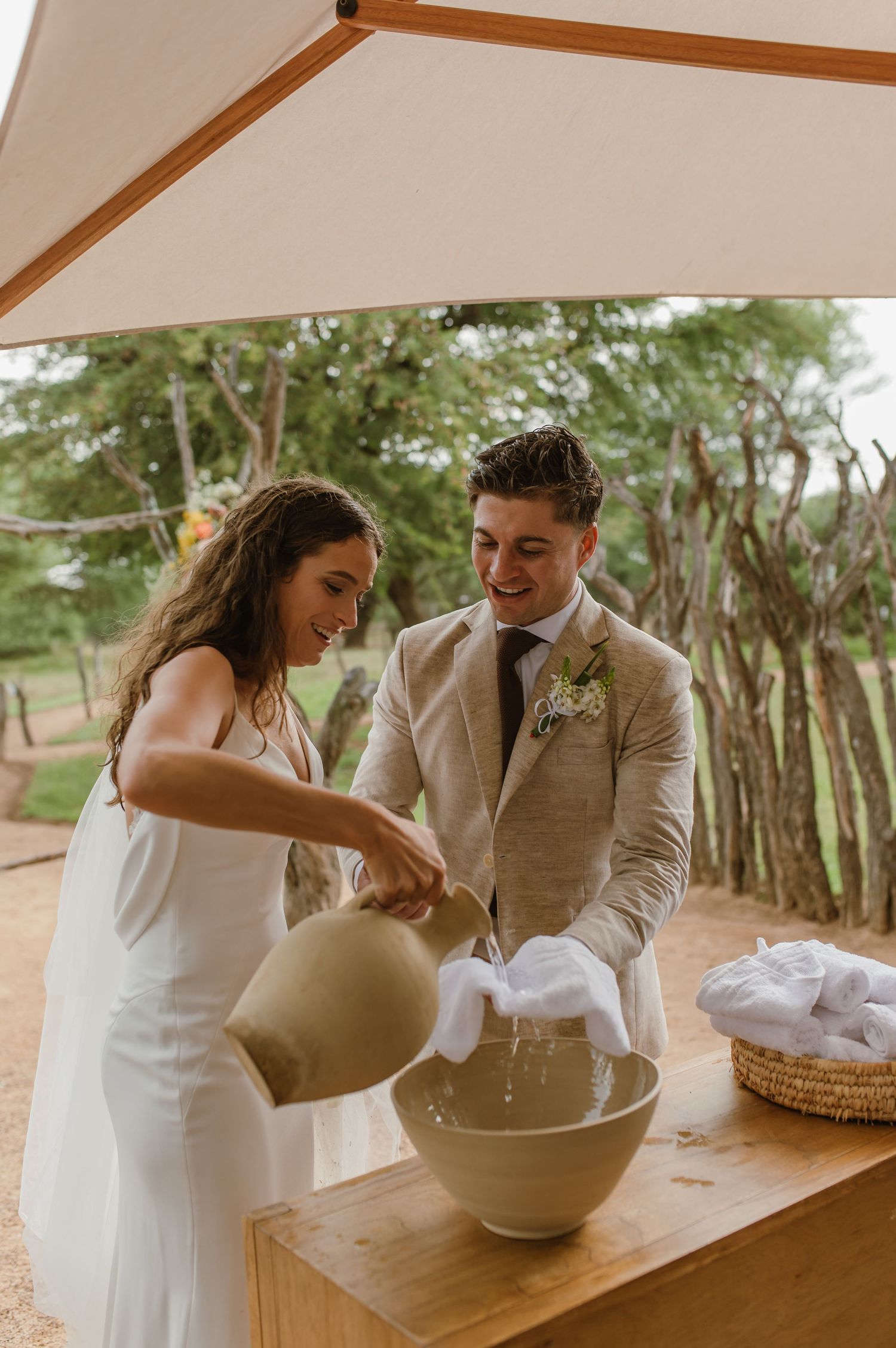 Wedding couple participates in a ceremonial ritual with a large vessel at an outdoor venue.