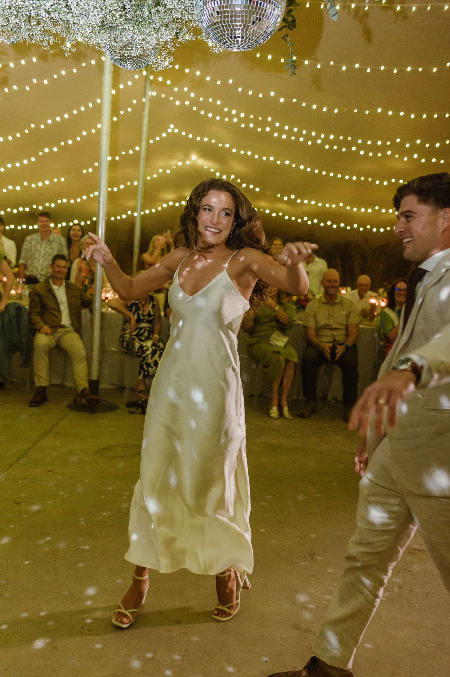 Dancers perform lively moves on the reception floor under glowing string lights.