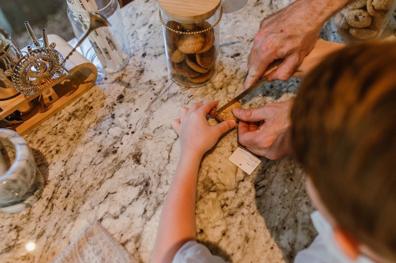 Adult and child hands working together on cookies at a marble kitchen counter.