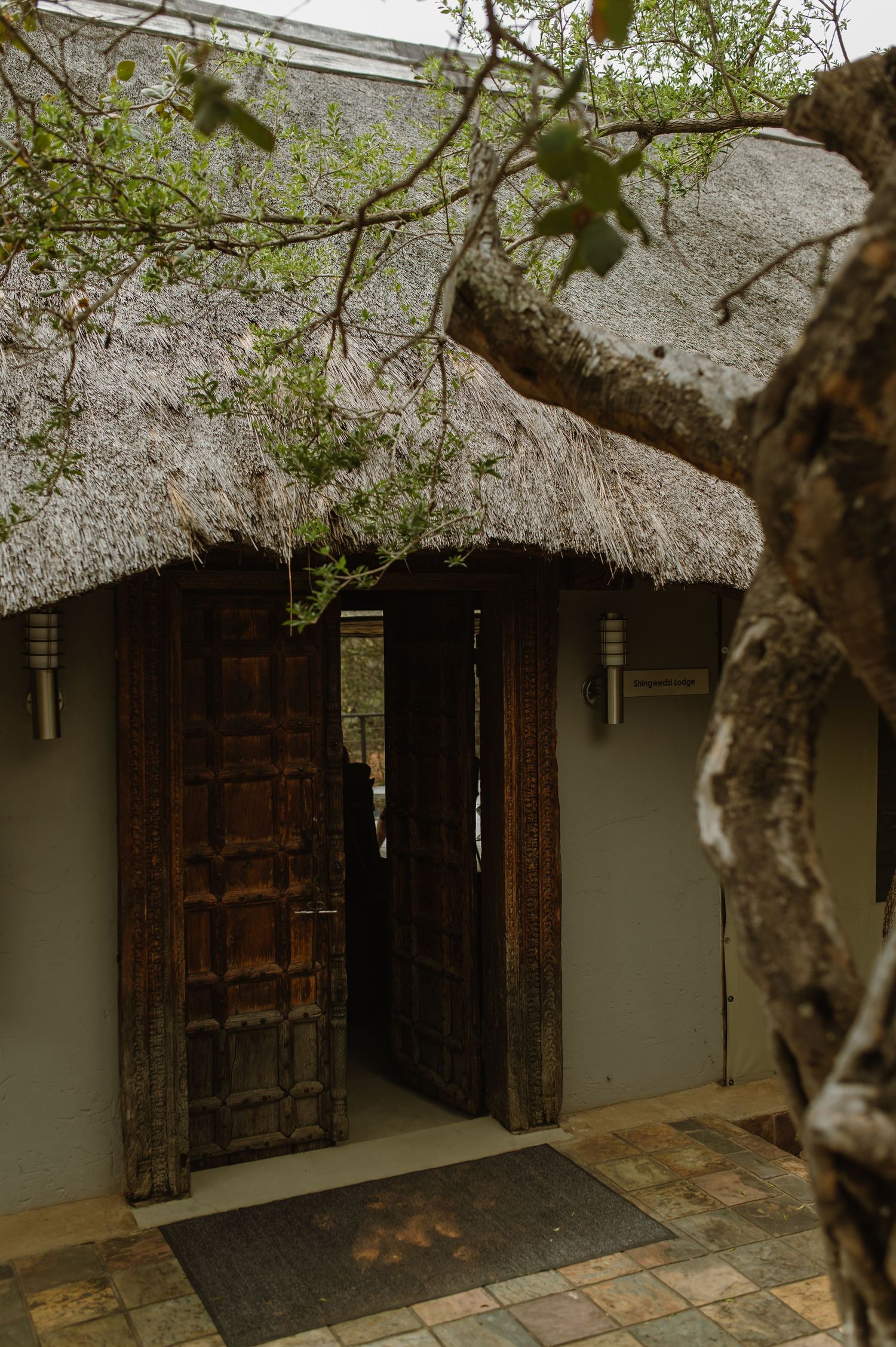 Rustic thatched roof entrance with ornate wooden doors and stone pathway at an African safari lodge.
