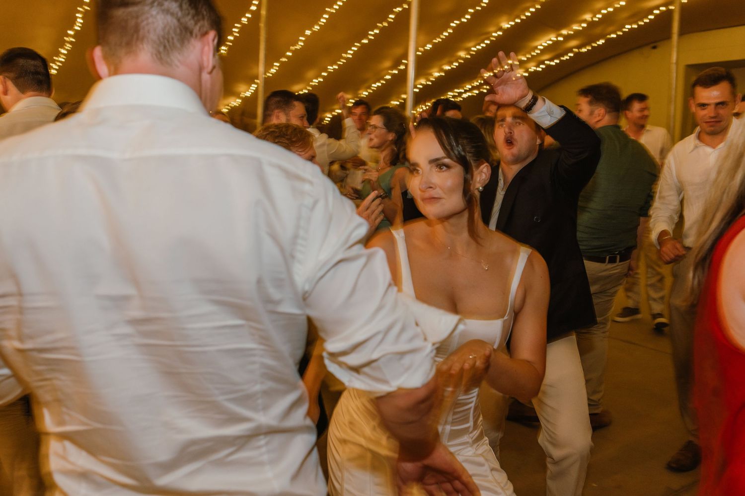 Guests dancing and celebrating at a lively wedding reception under twinkling lights.