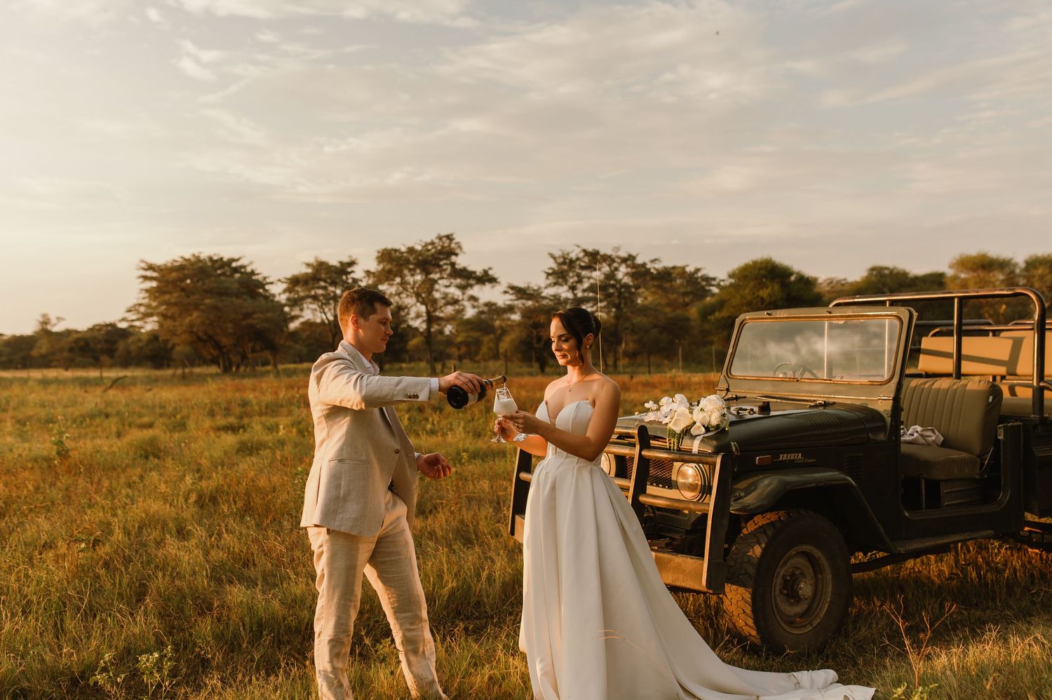 A romantic wedding photoshoot in a field with a vintage military vehicle silhouetted against the sunset.