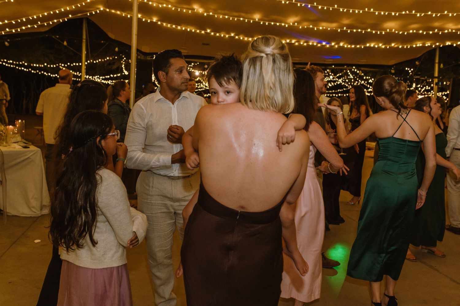 Wedding reception dance floor filled with guests enjoying themselves under warm string light decorations.