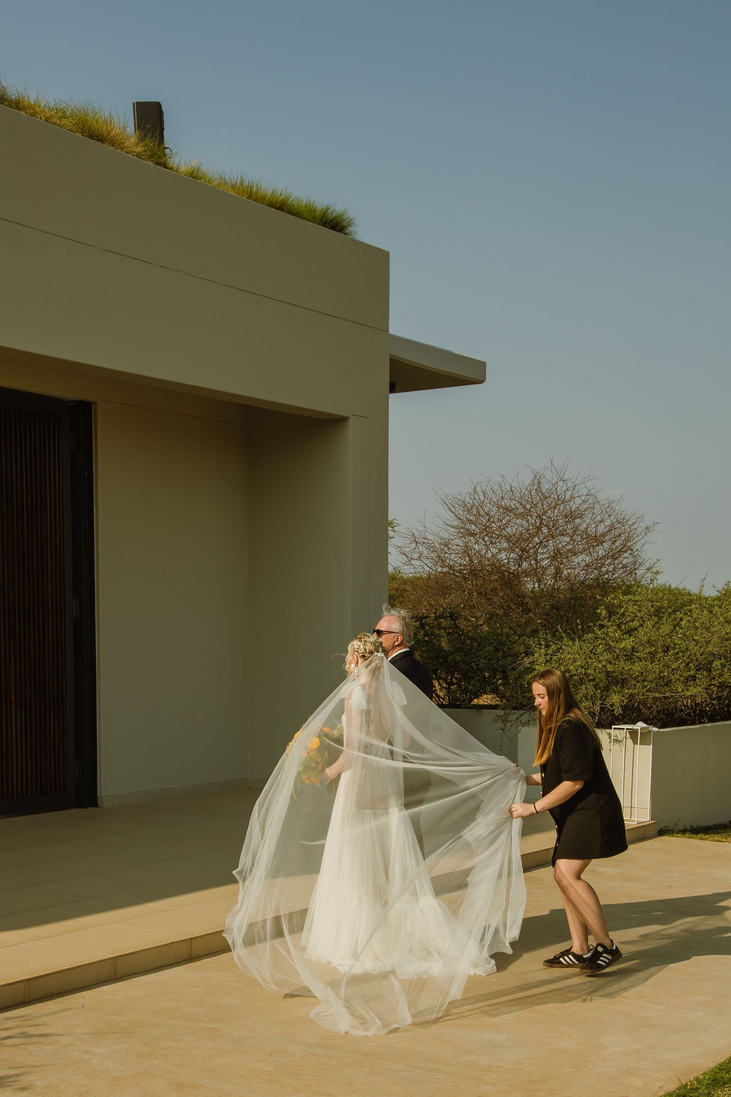 Wedding preparation scene with flowing white veil being arranged outdoors.