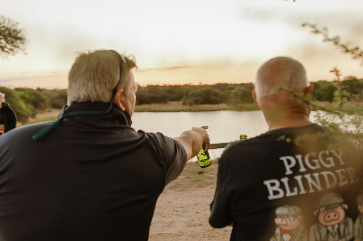Group wearing t-shirts with text standing together at sunset near water.